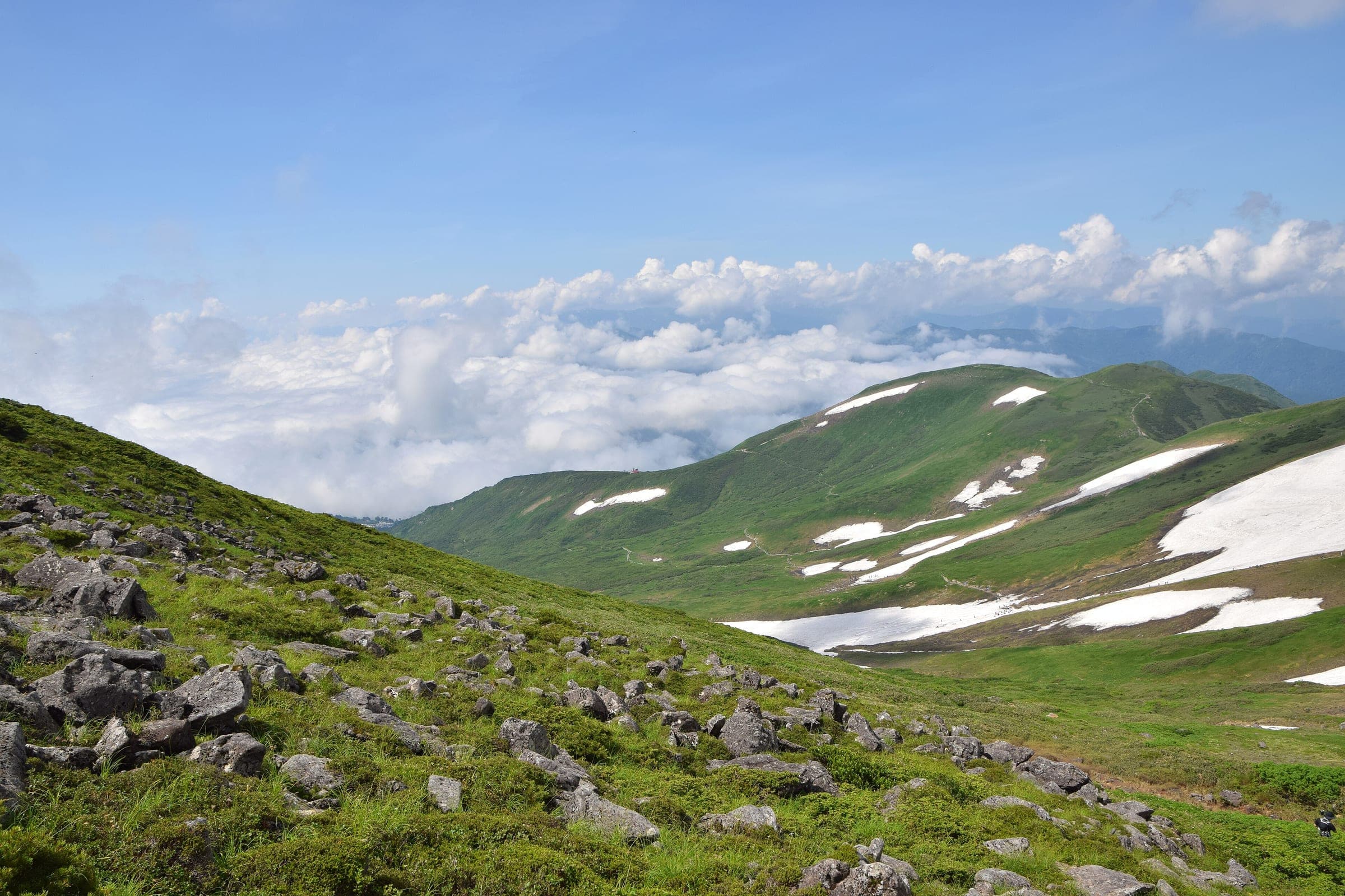 Late snowfields still streak the green flanks of Mount Gassan in July above a sea of cloud.