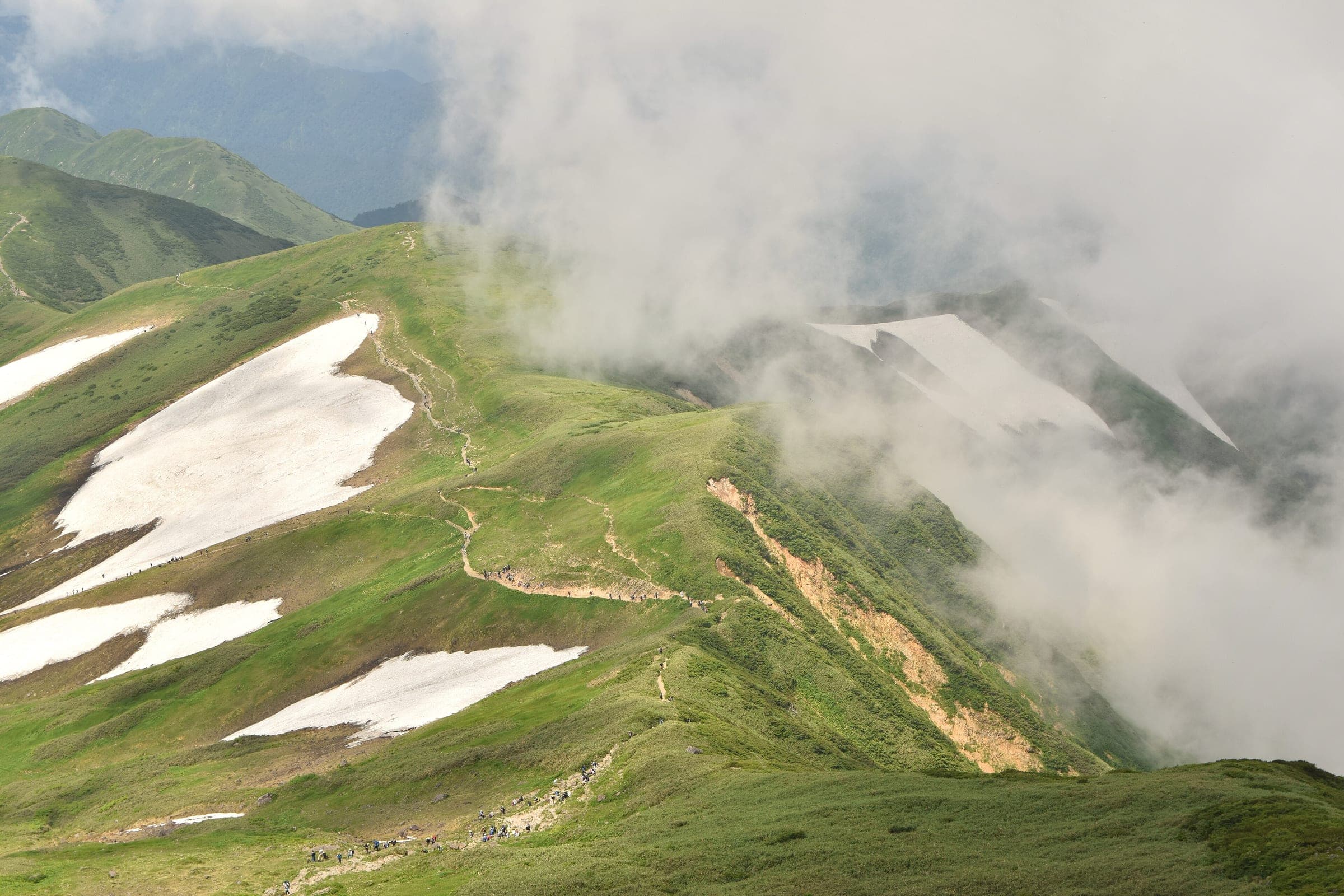 Cloud spills over a Gassan ridge where snow patches linger beside the hiking trail in July.