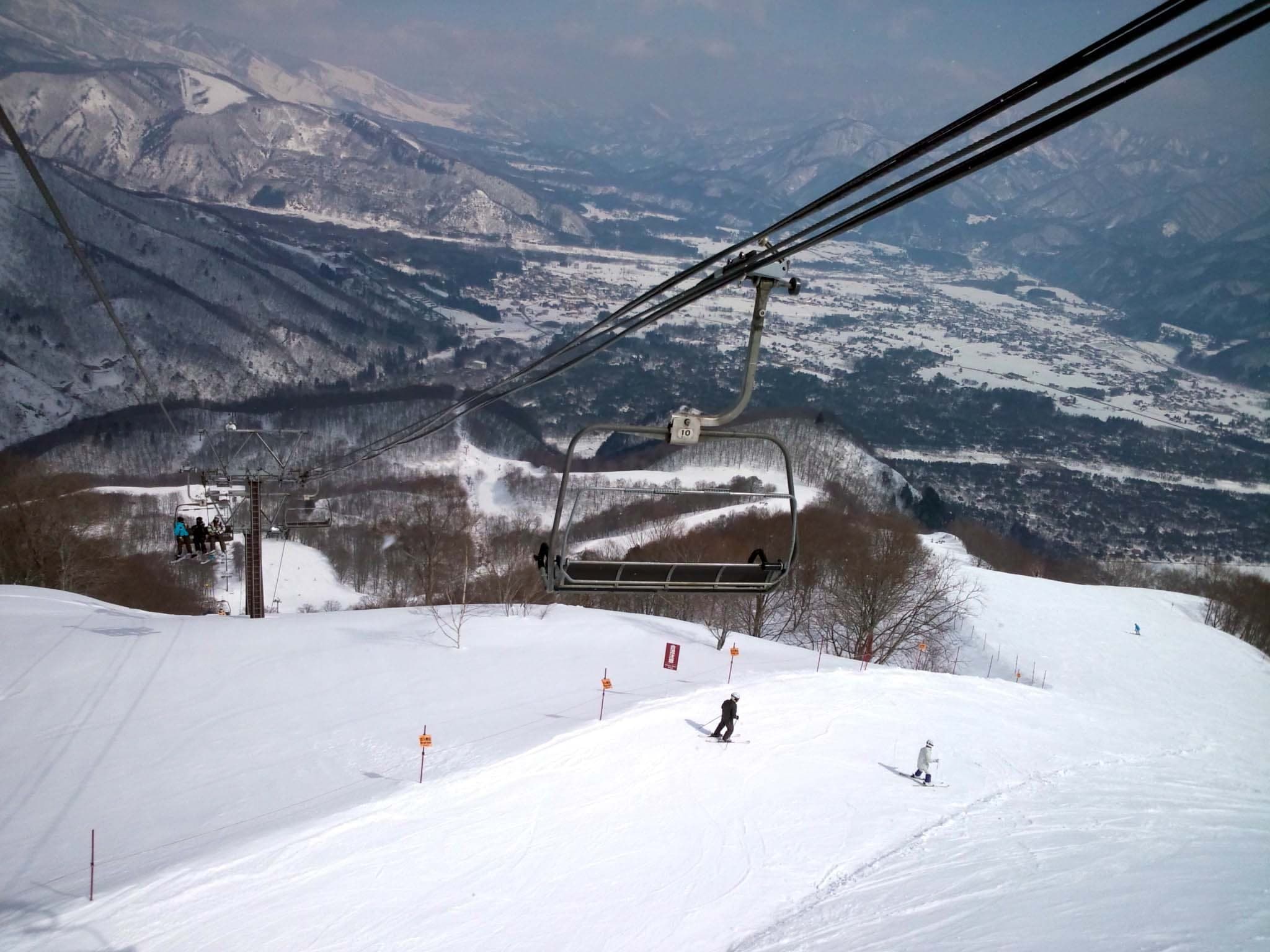 A Hakuba47 chairlift climbs over riders with the Hakuba valley far below