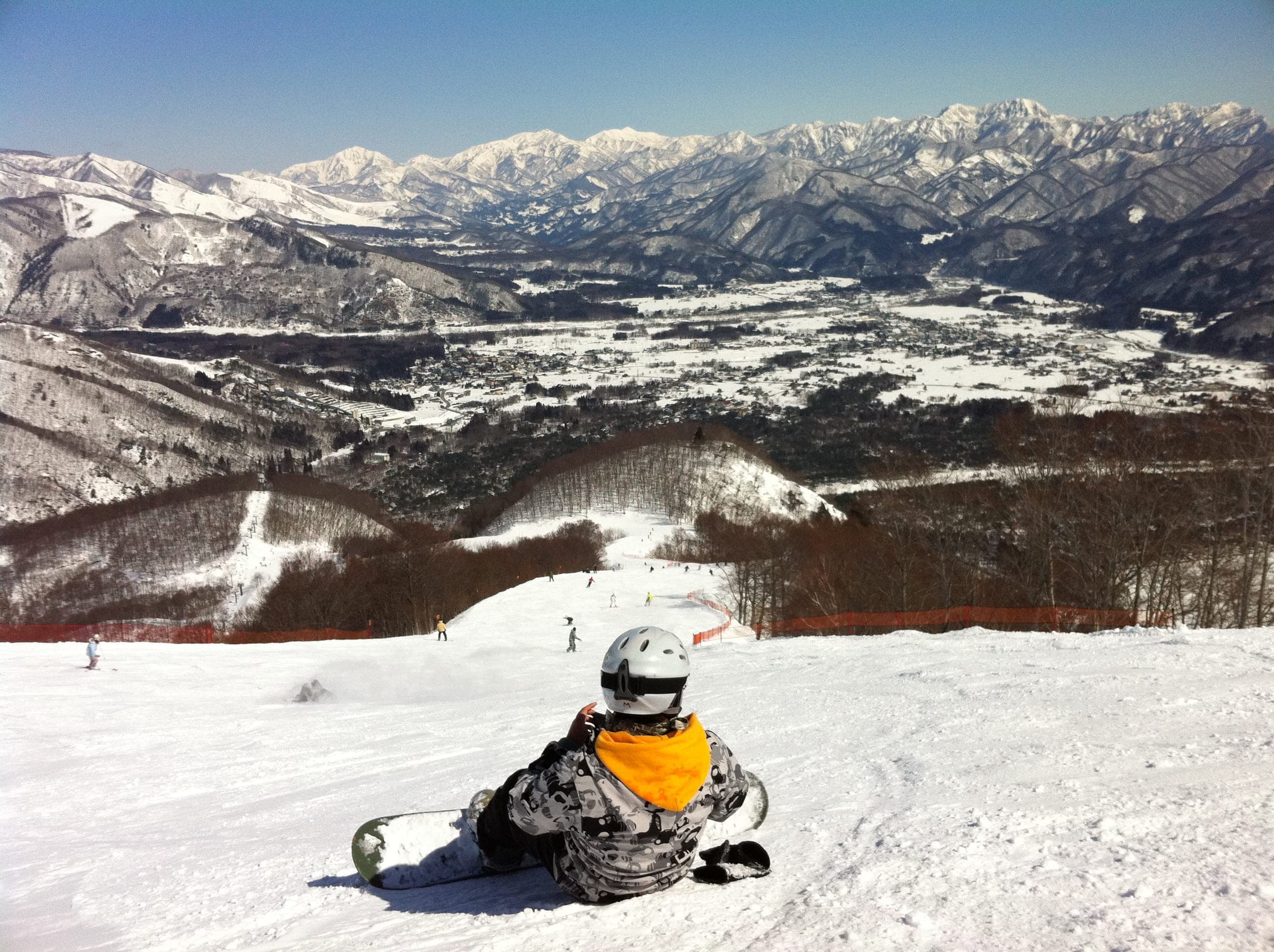 A snowboarder sits on a Hakuba47 run above the Hakuba valley on a clear March day
