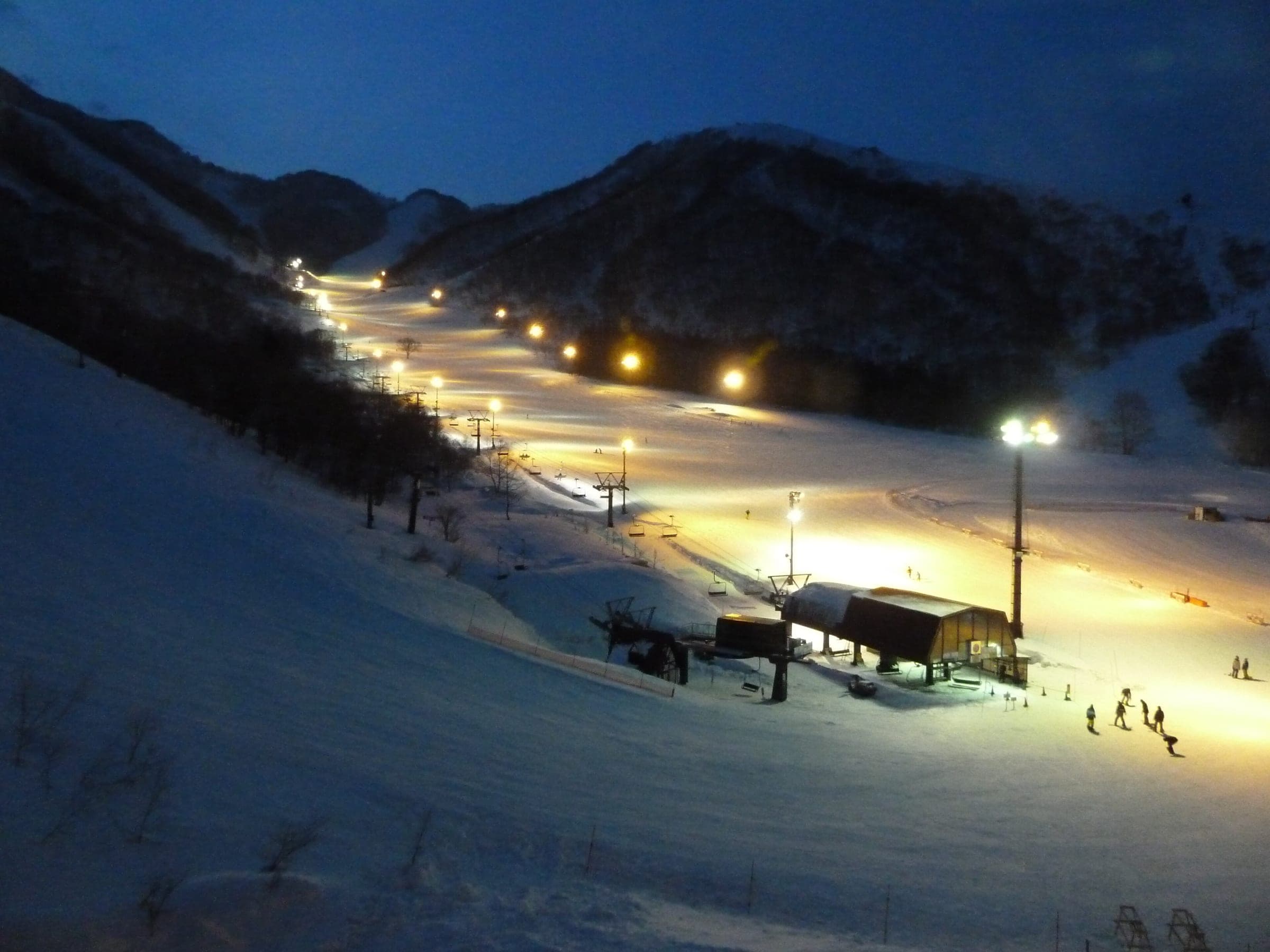 Floodlights trace the runs of Hakuba Cortina at dusk as riders gather near the base lift