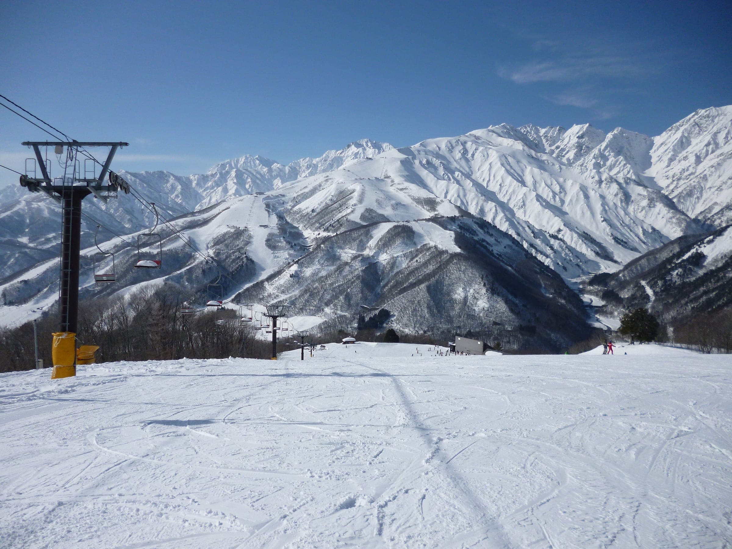 A chairlift reaches the top of Hakuba Iwatake with the Hakuba range across the valley
