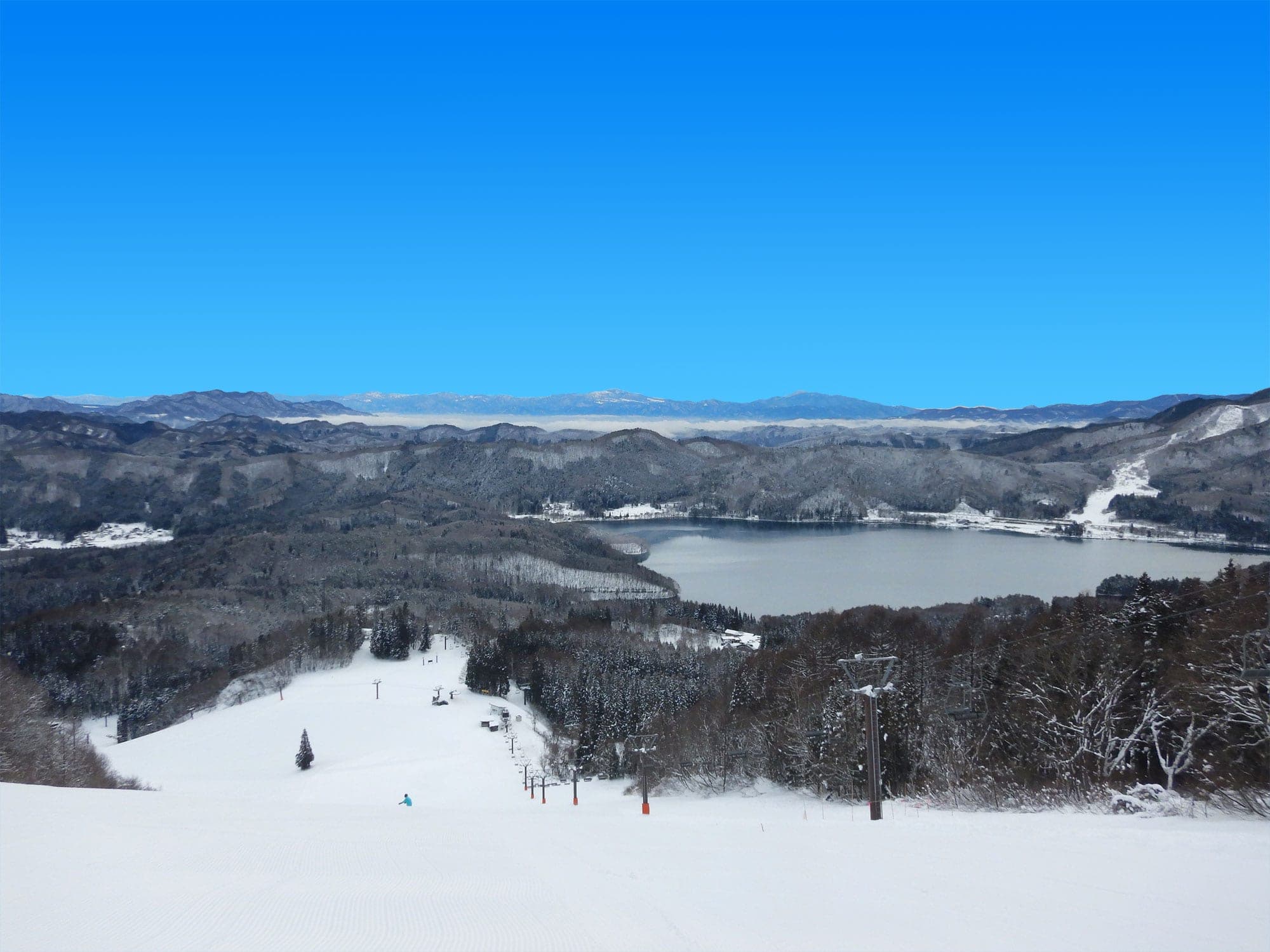 A groomed run at Hakuba Sanosaka drops toward Lake Aoki under a clear winter sky