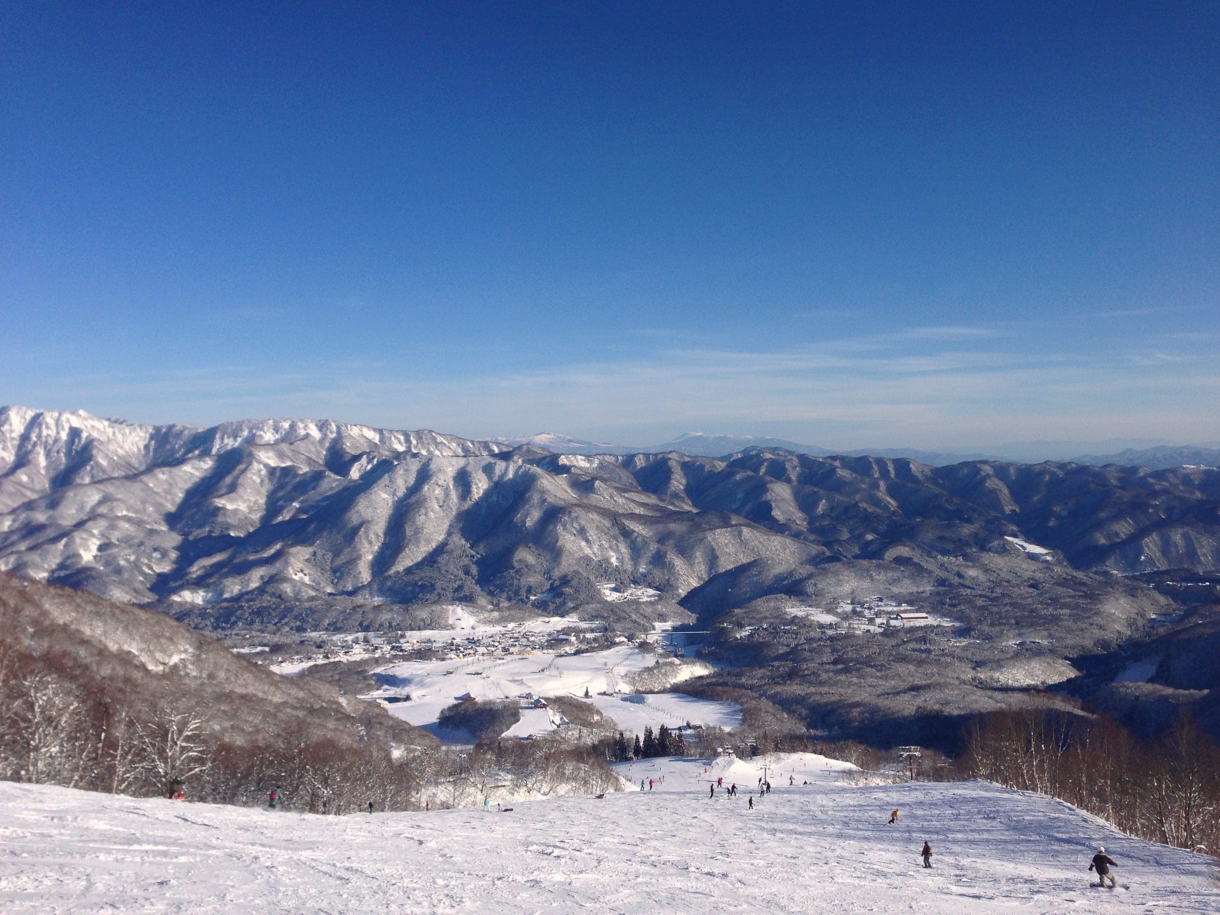 Skiers head down a sunny run at Tsugaike Mountain Resort with snowy ridges across the valley