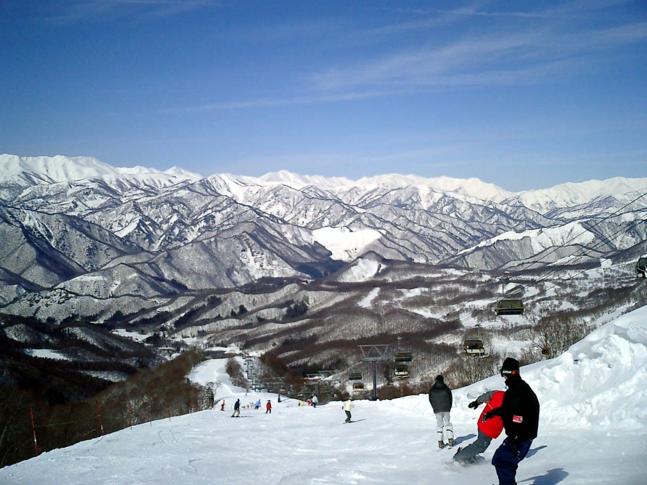 Riders at Hodaigi stop above the lifts with snowy ranges on the Niigata border beyond