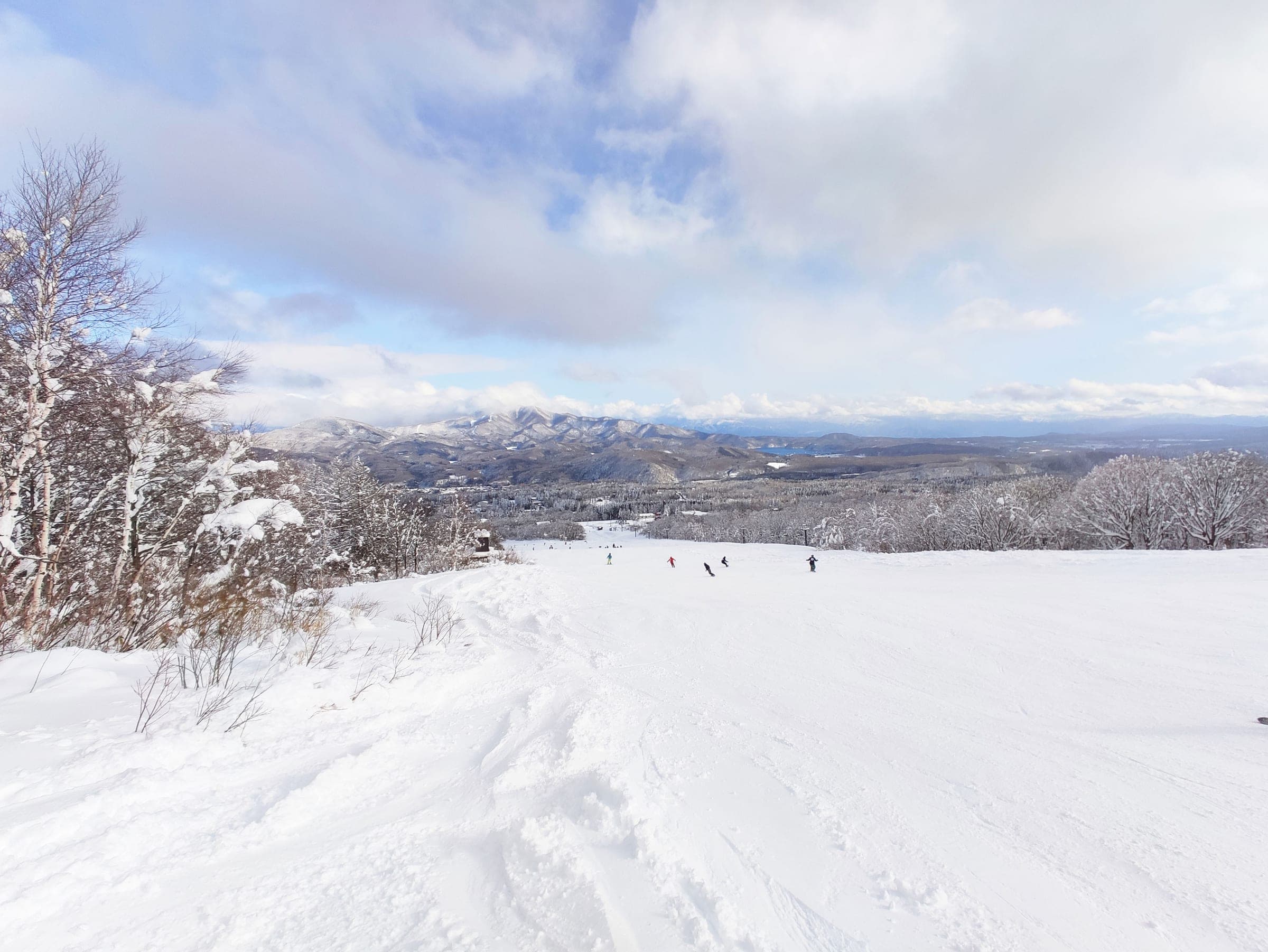 Skiers descend the wide Kayaba slope at Ikenotaira Onsen under a bright February sky