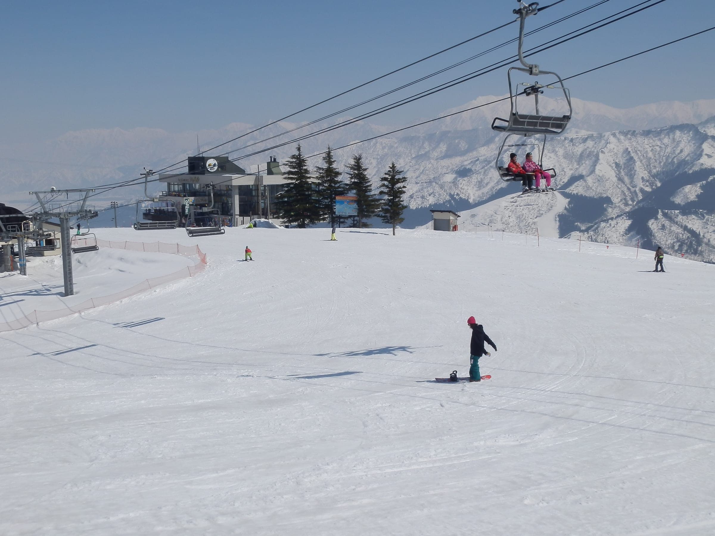 A snowboarder crosses a sunny top station run at Ishiuchi Maruyama beneath a chairlift