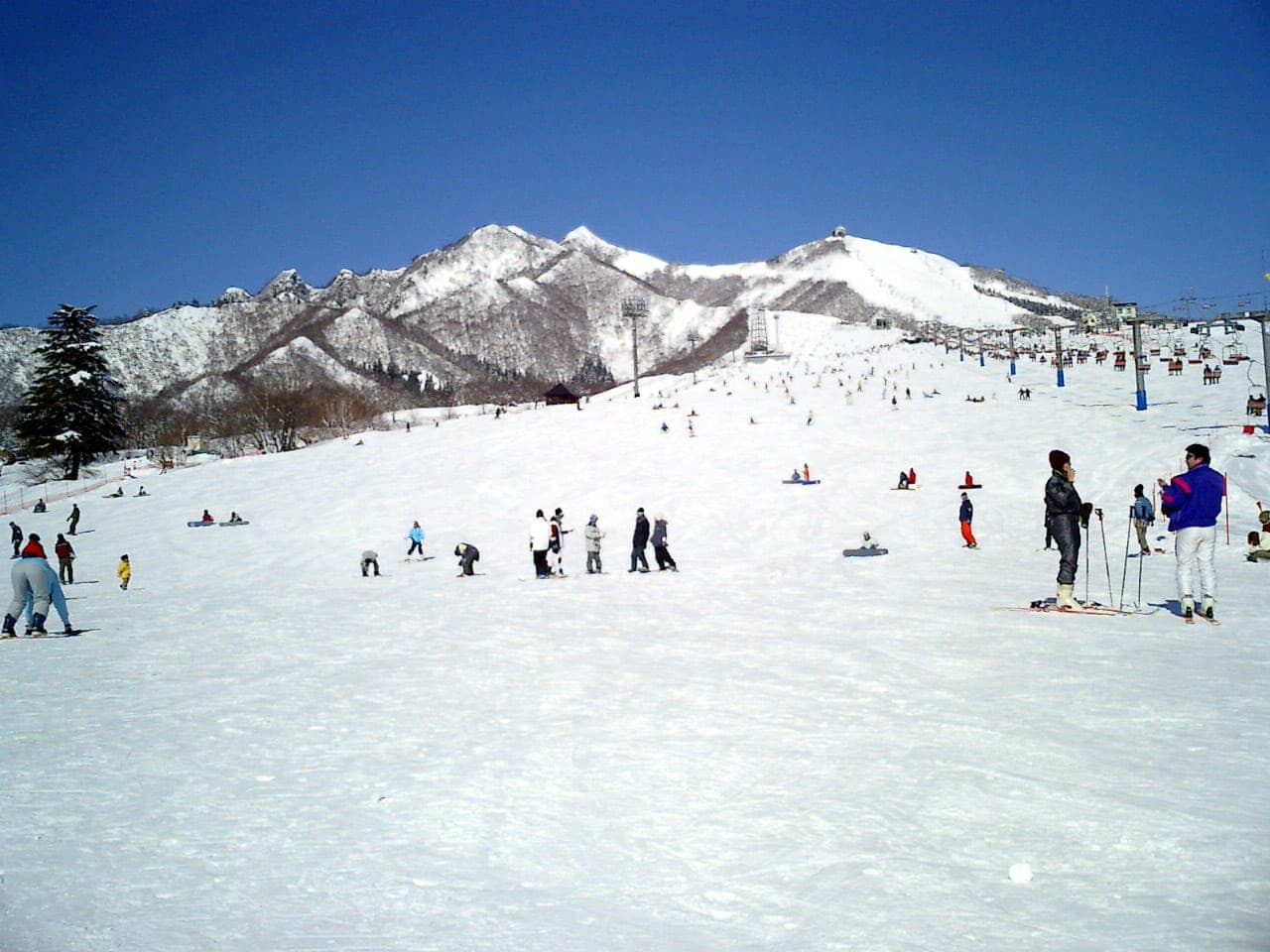 Skiers and snowboarders gather on the broad lower slope at Iwappara below a rocky ridge