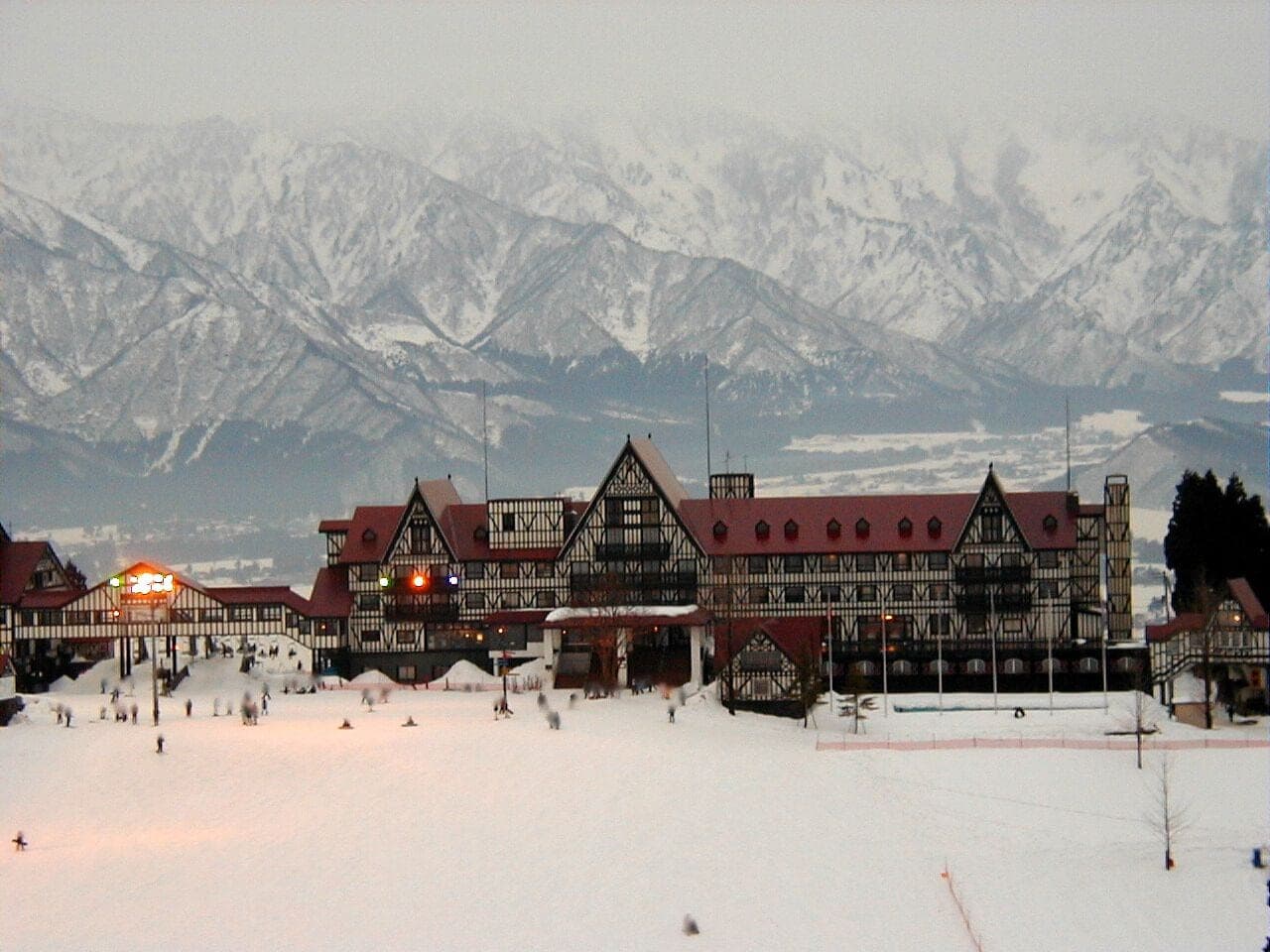 The half-timbered hotel at the foot of Joetsu Kokusai glows at dusk below the Echigo mountains
