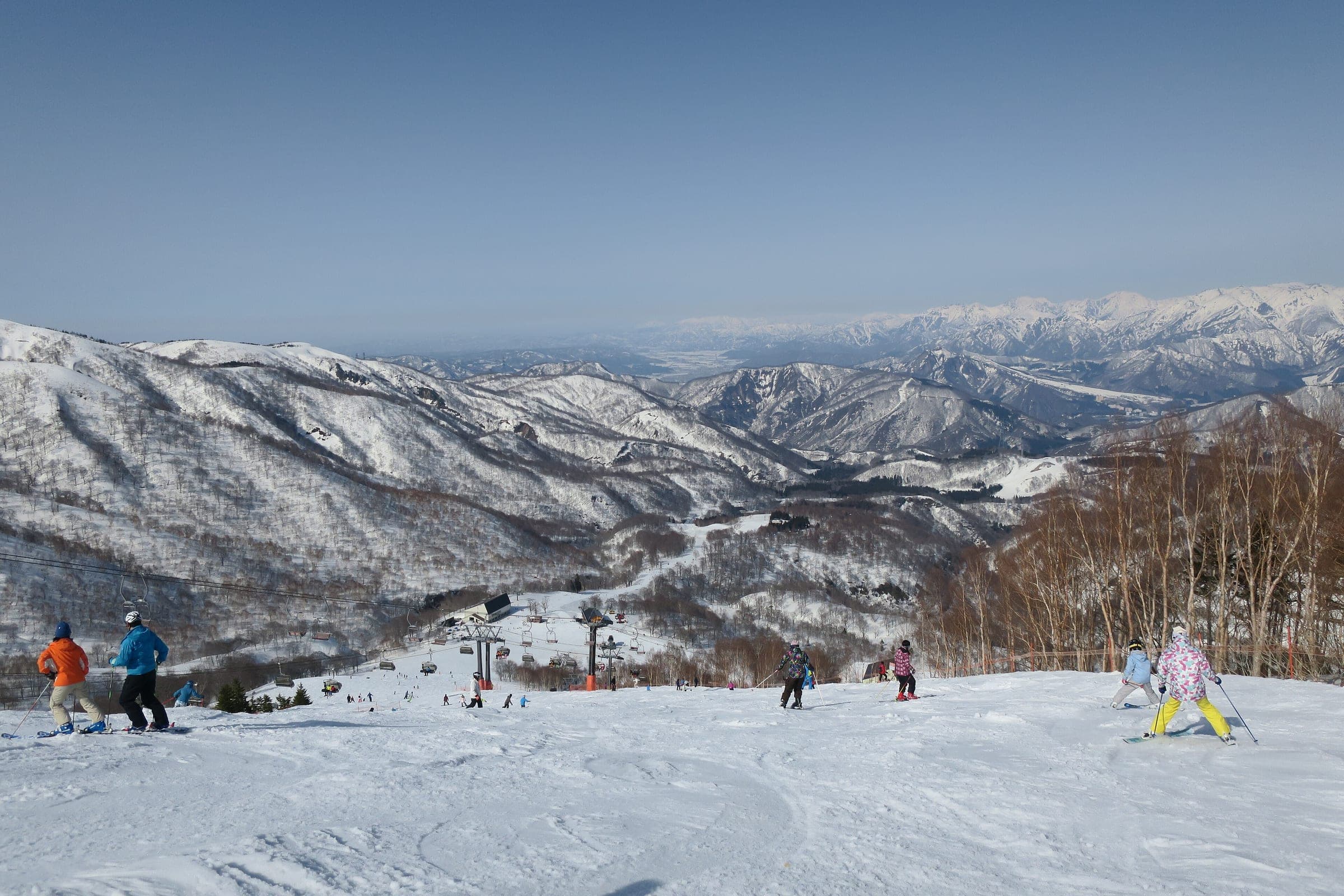 Skiers and snowboarders head down a groomed run at Kagura with the Echigo ranges beyond