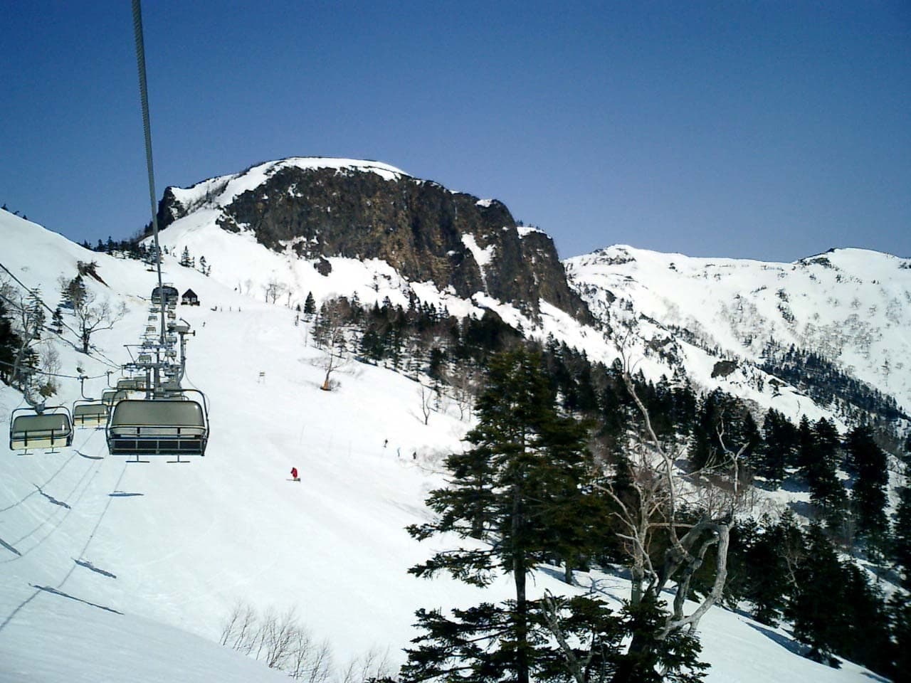 A chairlift at Kawaba climbs toward a rocky summit in clear spring sunshine