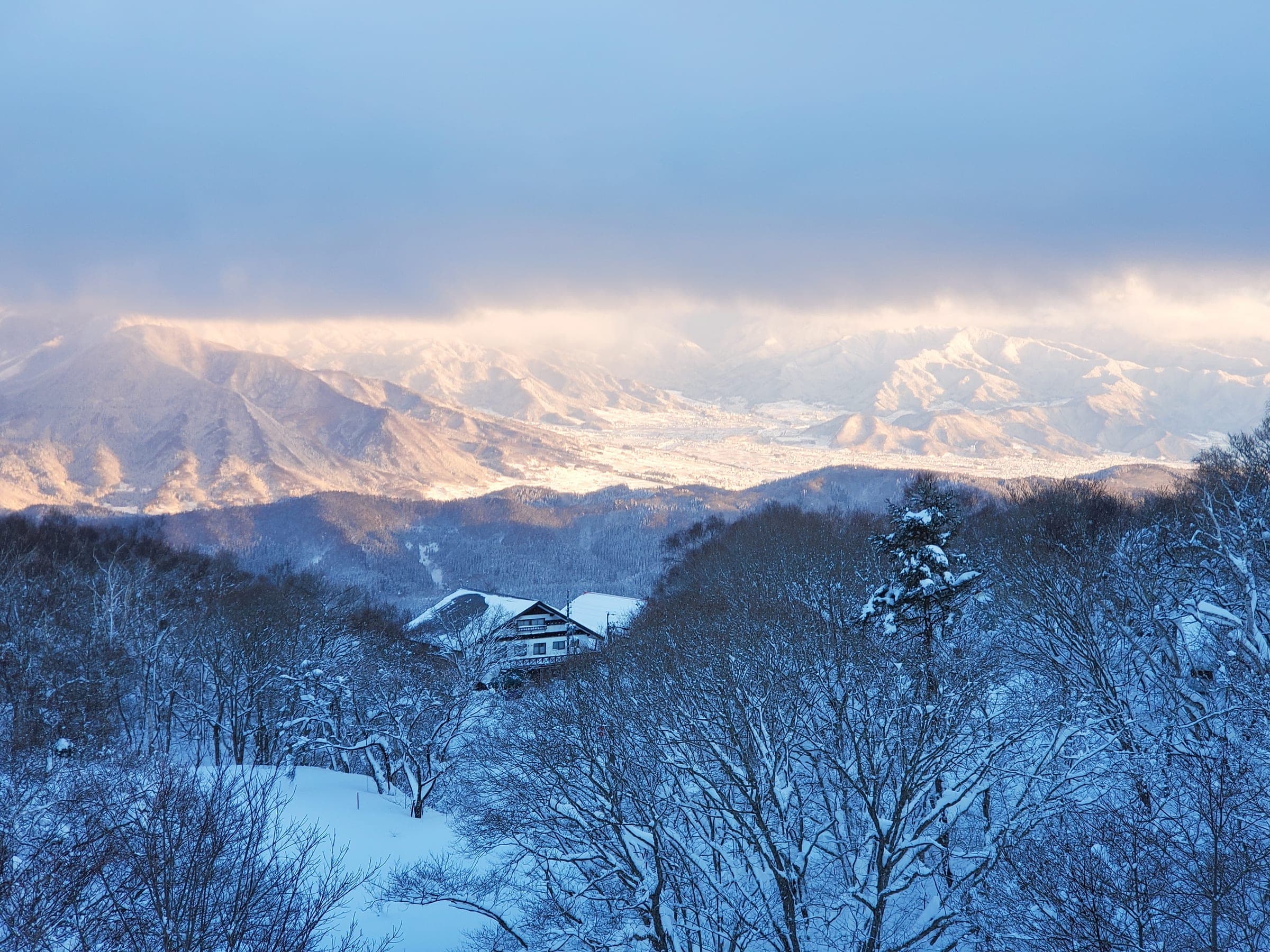 Low winter sun lights the snowy ridges beyond the frosted forest of Madarao Kogen