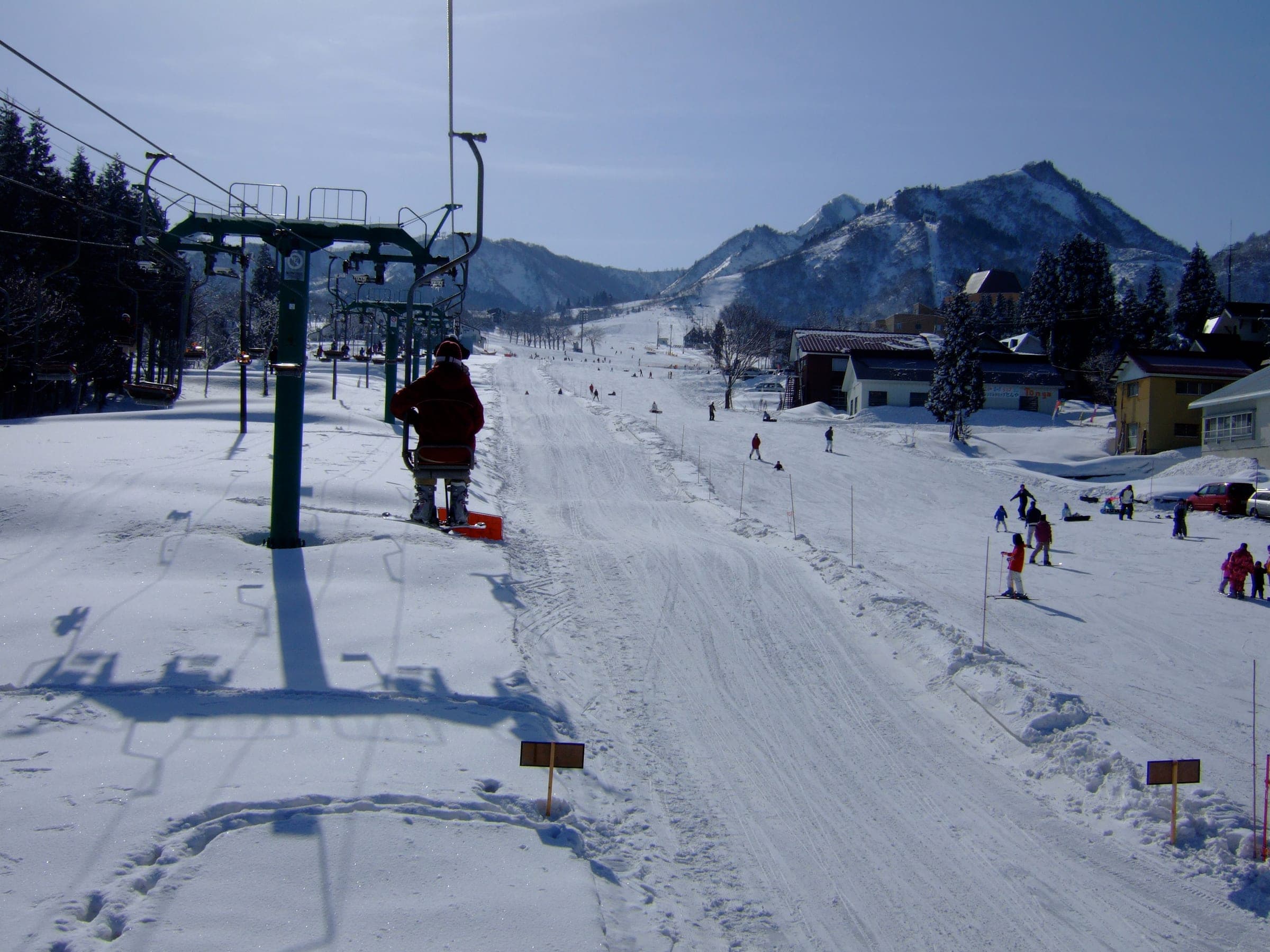 A chairlift rises over a groomed run at the base of Maiko with jagged peaks behind