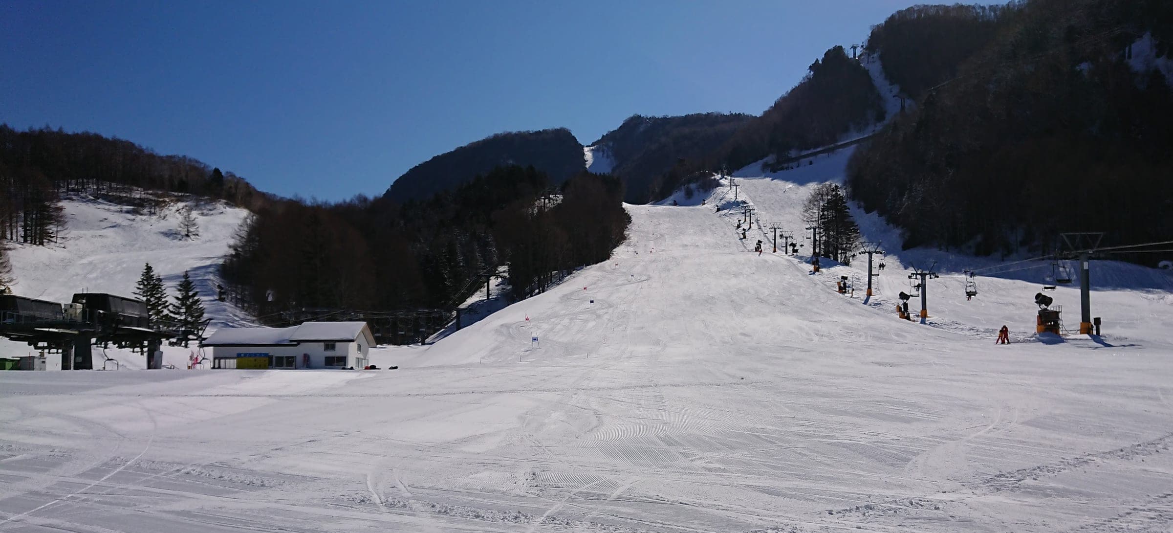 Groomed lower slopes at Marunuma Kogen rise toward the chairlifts on a clear March day