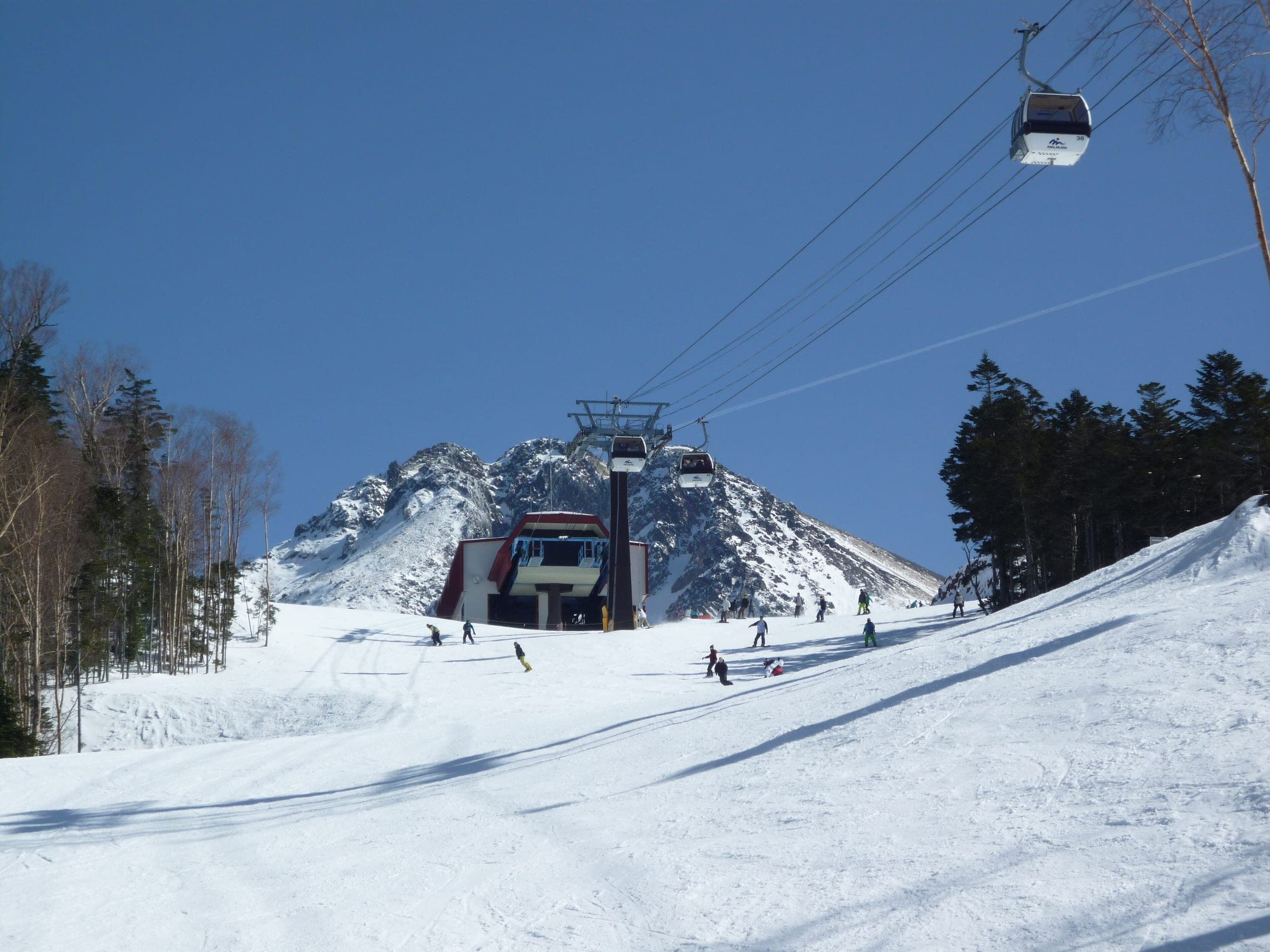 Riders carve below the Marunuma Kogen ropeway as gondolas climb toward a rocky peak