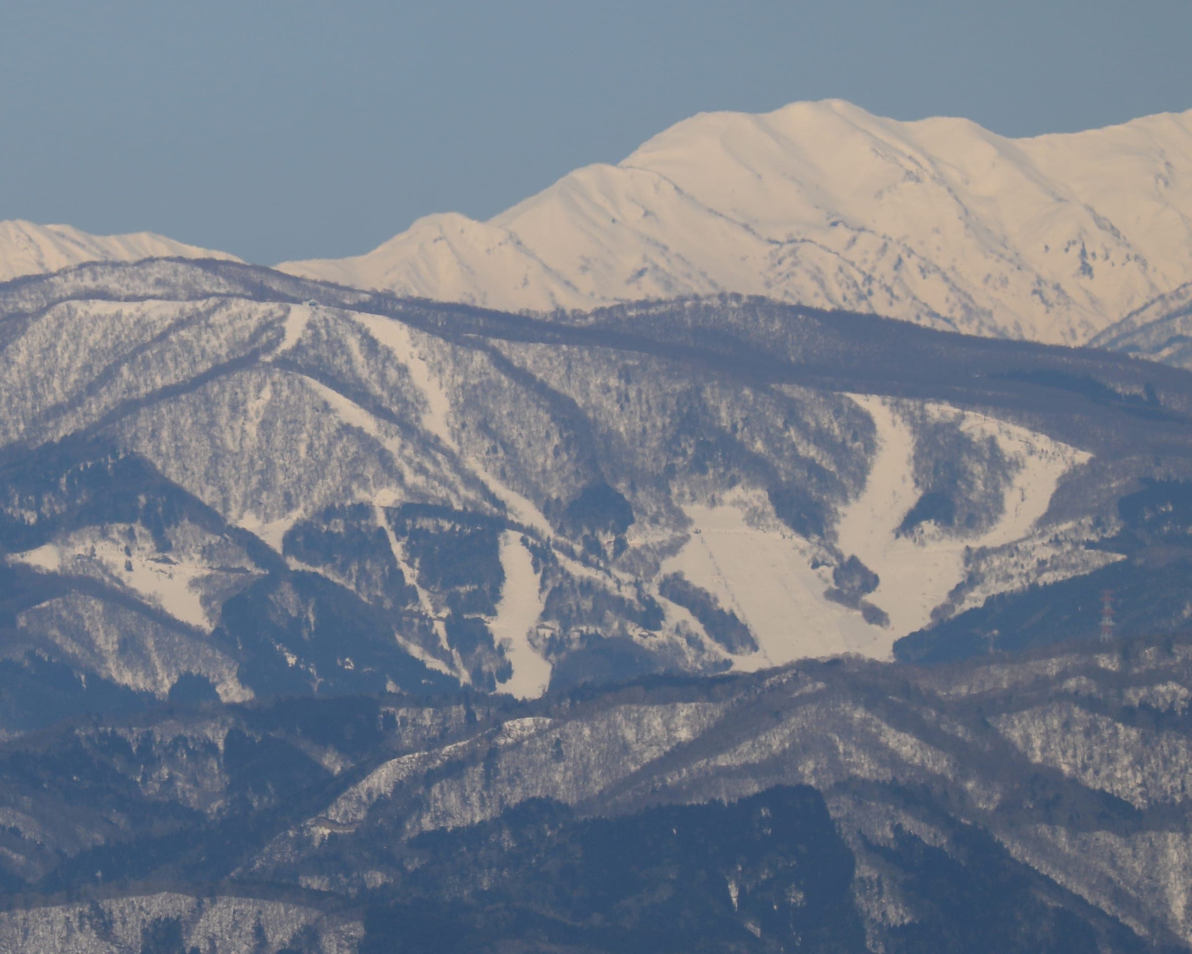 Meiho Snow Resort's runs cross a snowy ridge below the white peaks of the Ryohaku range