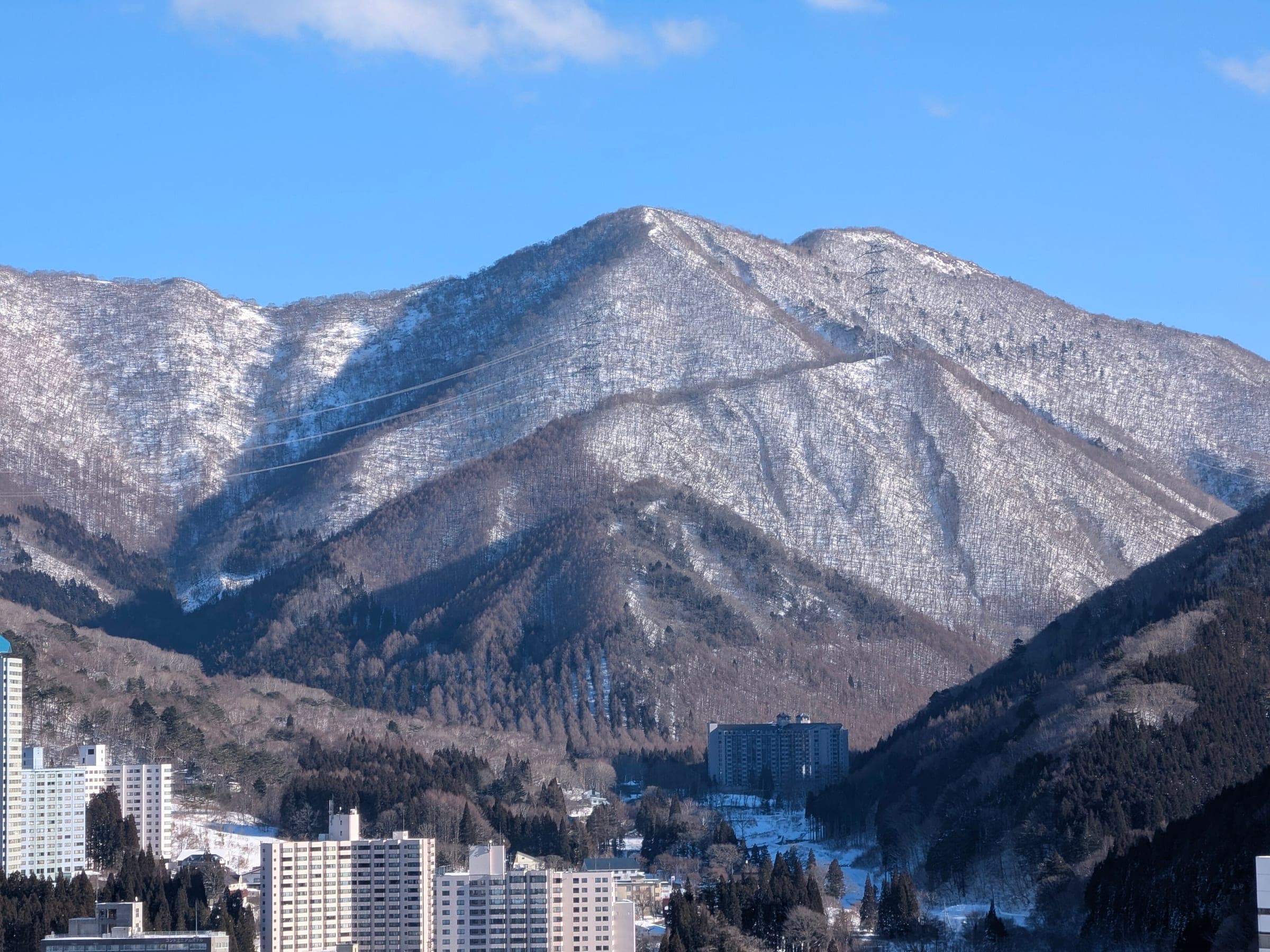 A snow-streaked ridge rises over the hotel blocks of Naeba on a clear January day