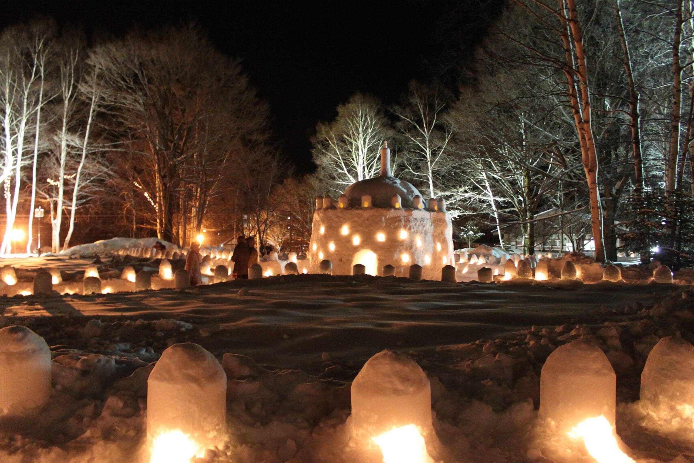 Snow lanterns glow beneath the bare birches of Nikko Yumoto Onsen on a winter night