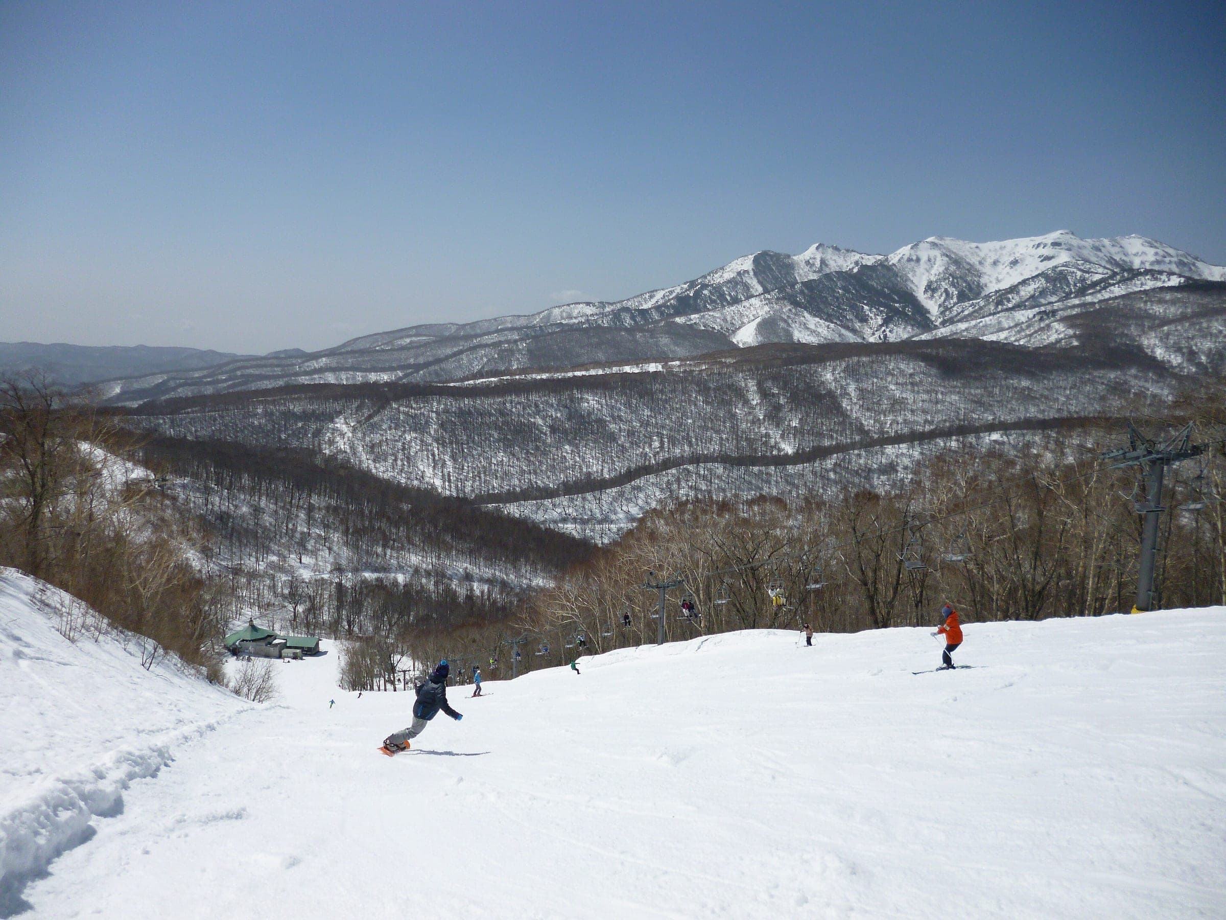 A snowboarder turns down Oze Iwakura with Mount Hotaka's snowy ridge across the valley