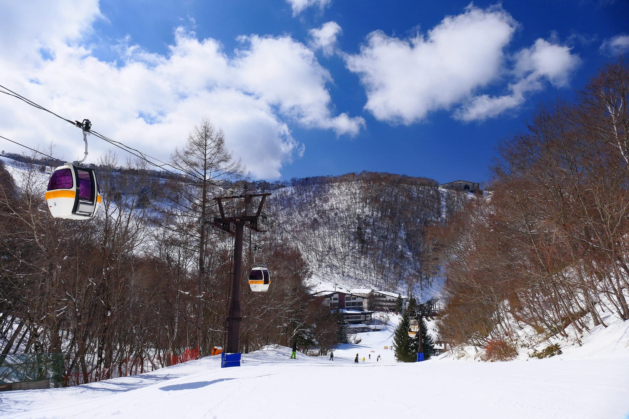 The Bunadaira gondola climbs over a groomed run at Shiga Kogen Hoppo Bunadaira under a bright sky