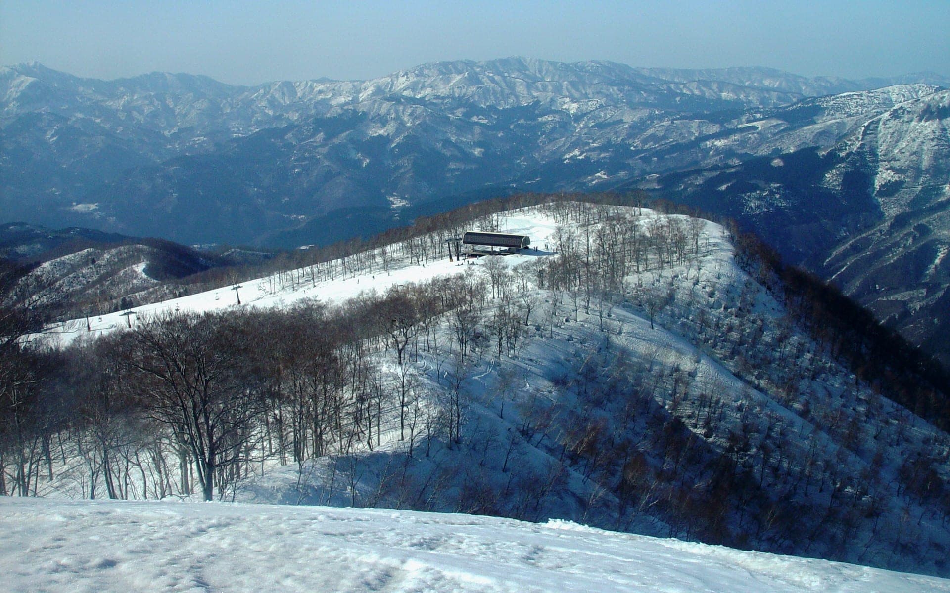A lift station tops a snowy ridge of Mount Hoonji at JAM Fukui Katsuyama with mountains of Fukui beyond