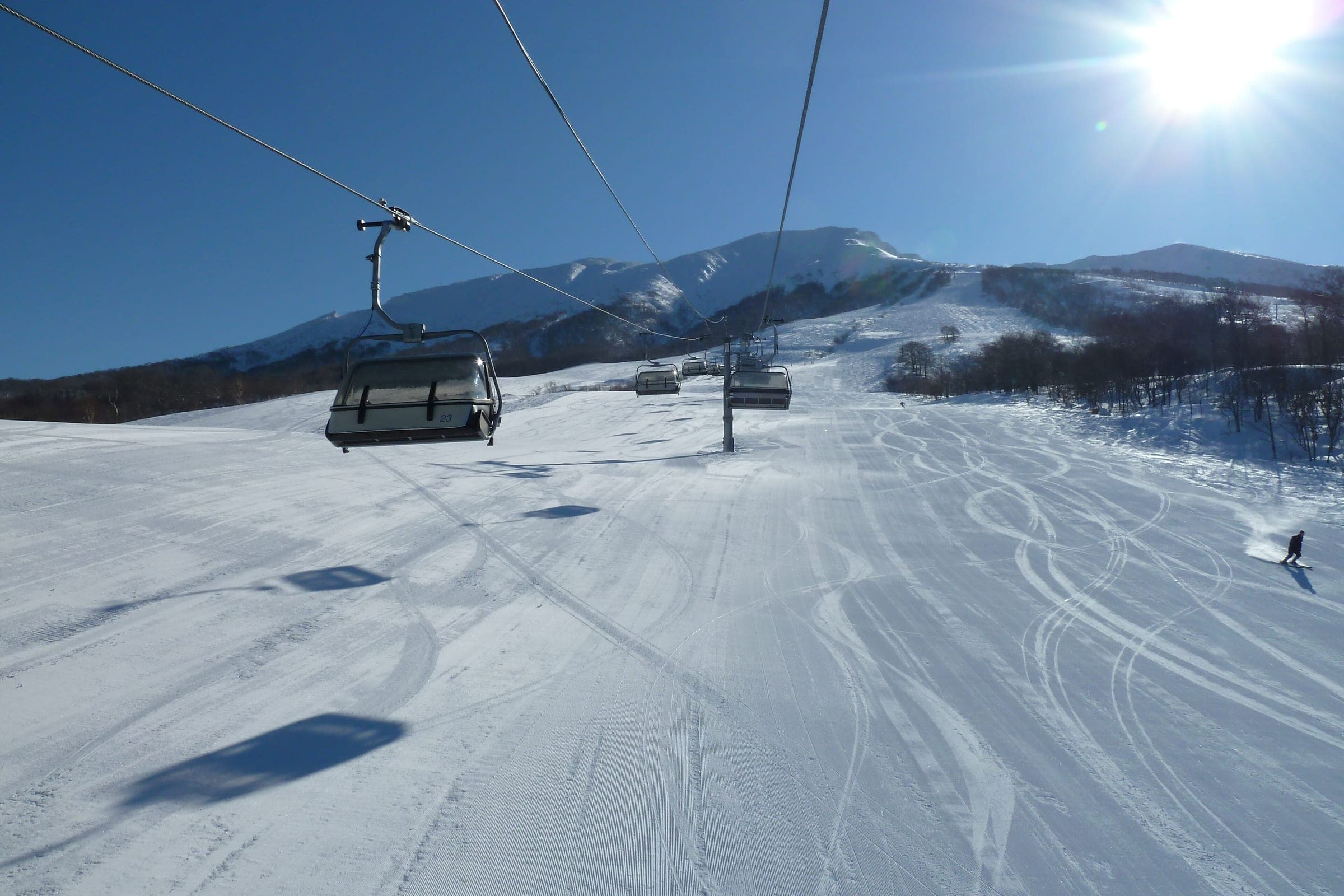 A snowboarder carves below the Kamoshika quad at Tazawako on a sunny winter morning.