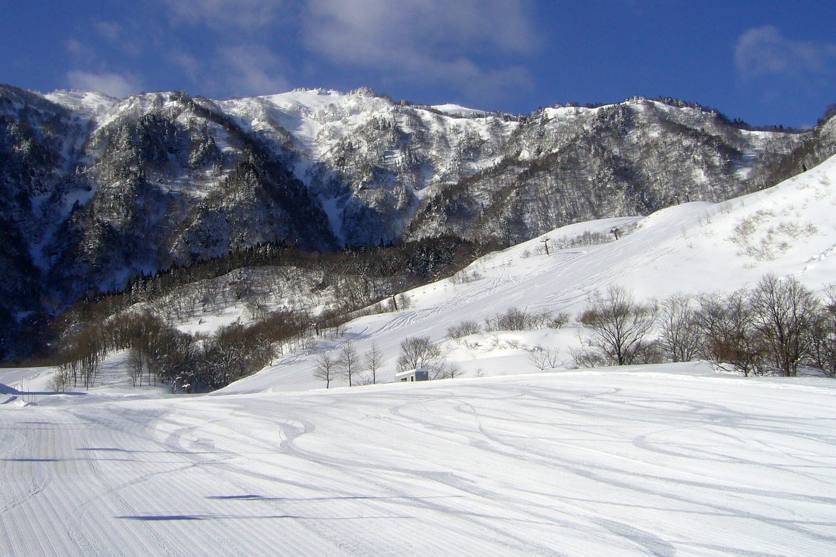 Mount Hyonosen's snowy ridge rises above groomed corduroy on a clear February day