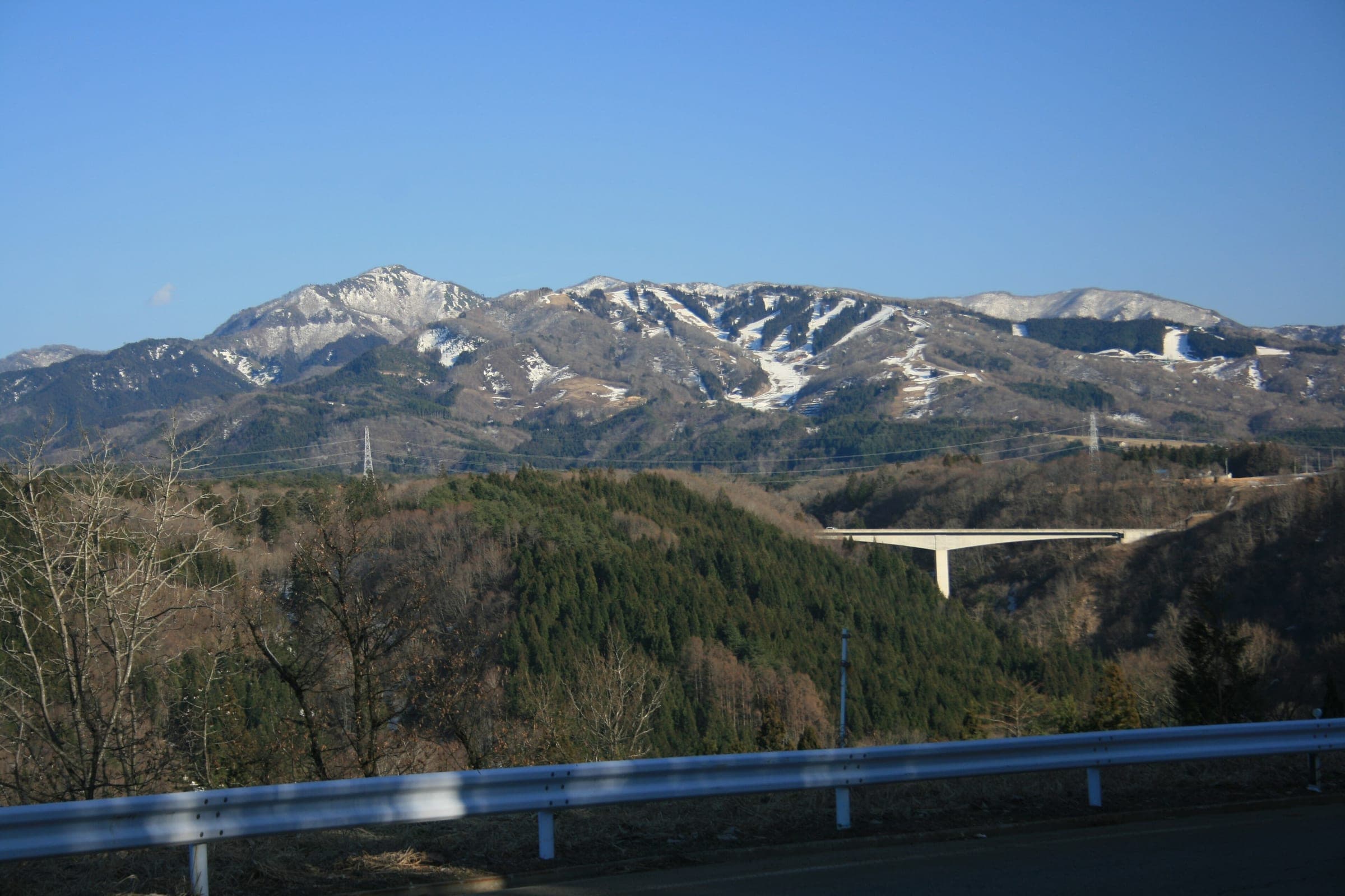 Ski runs streak the flanks of Mount Washi above an expressway bridge in the Hida highlands