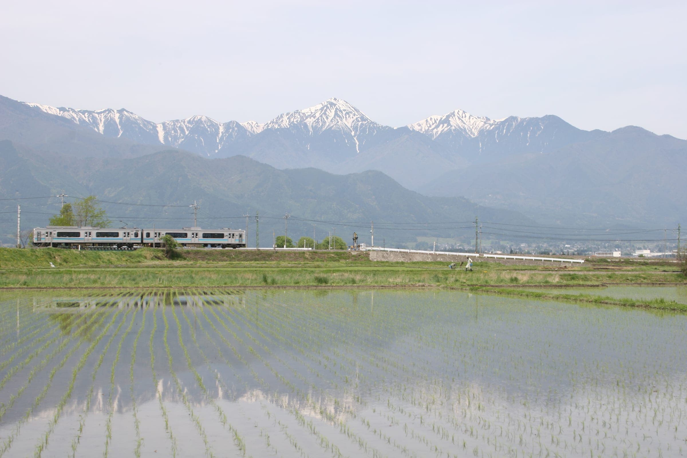 An Oito Line train crosses Azumino's flooded rice paddies below the snowy peaks around Mount Jonen
