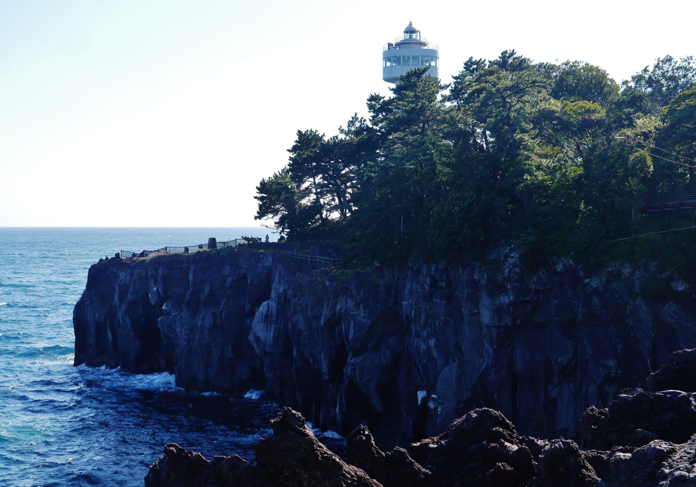 The Kadowaki lighthouse stands among pines above the black lava cliffs of the Jogasaki Coast near Ito