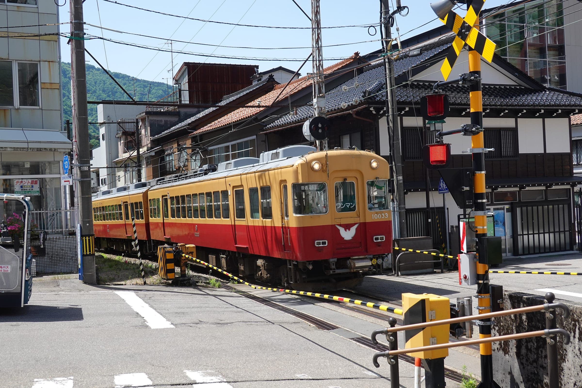 A red and cream Toyama Chiho Railway train pulls into Unazuki Onsen past a level crossing in May