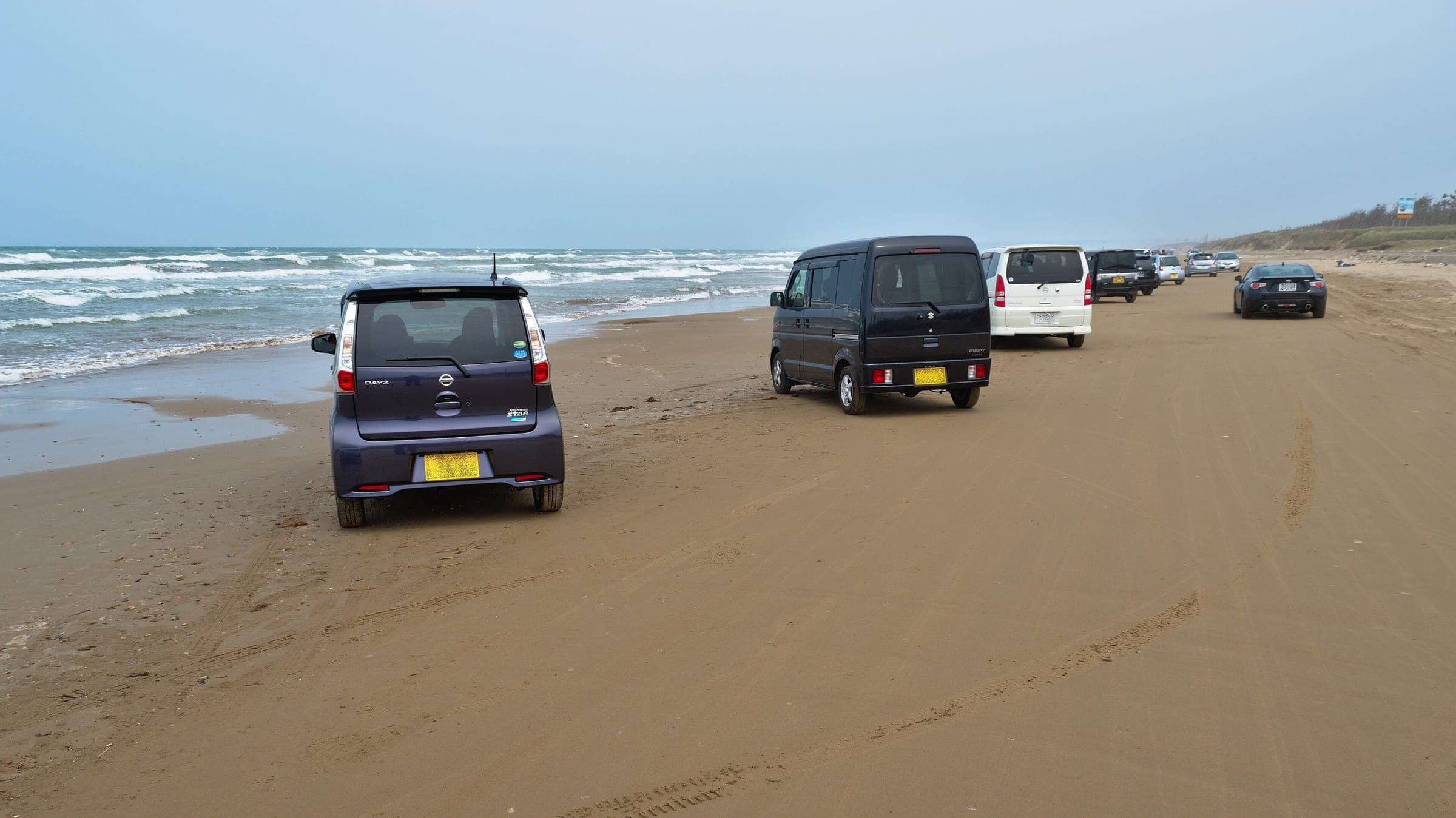 Cars drive along the firm sand of the Chirihama Nagisa Driveway beside the Sea of Japan in May