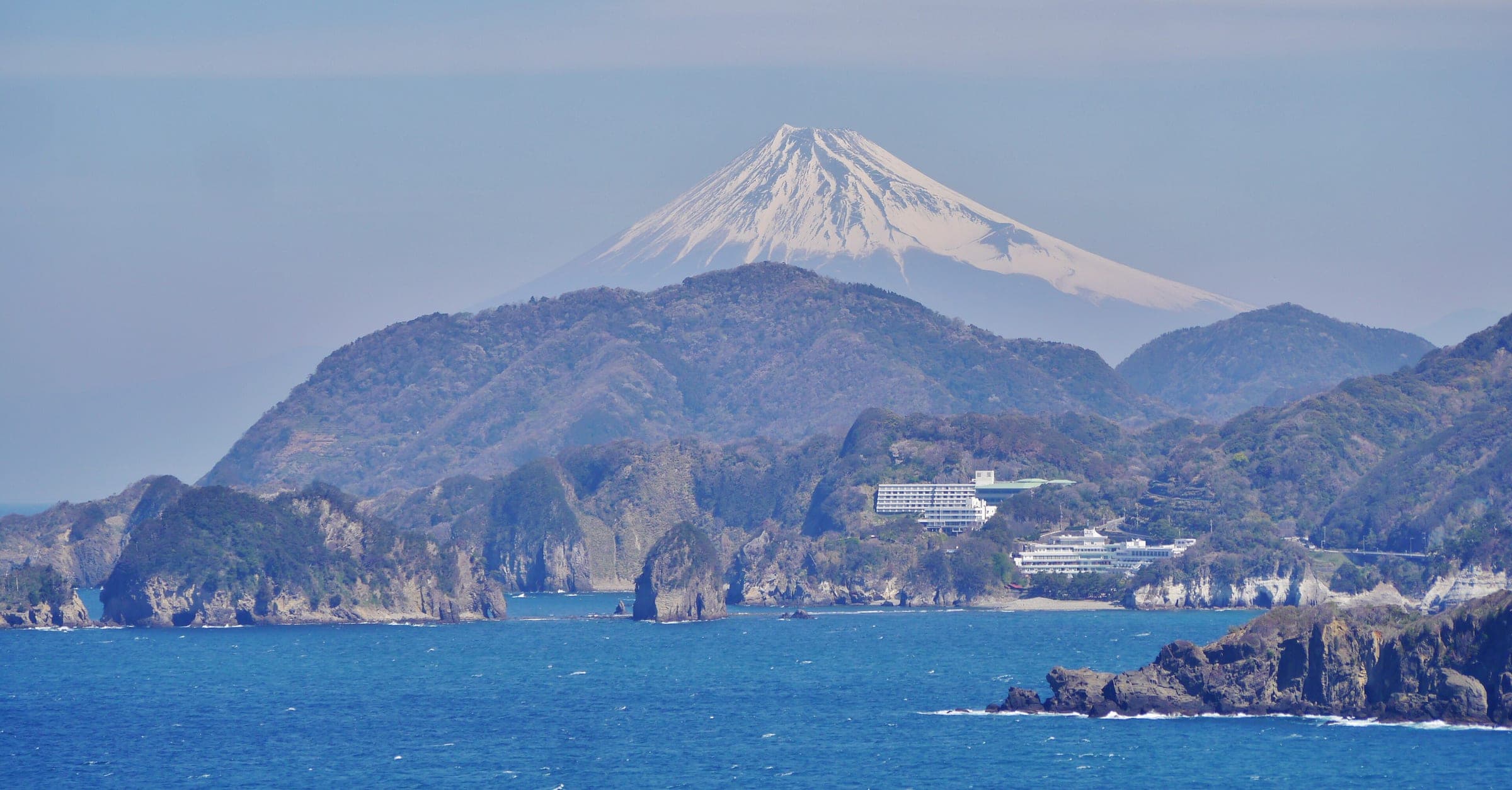 Snow-capped Mt. Fuji rises behind the cliffs and coves of the west Izu coast at Nishiizu.