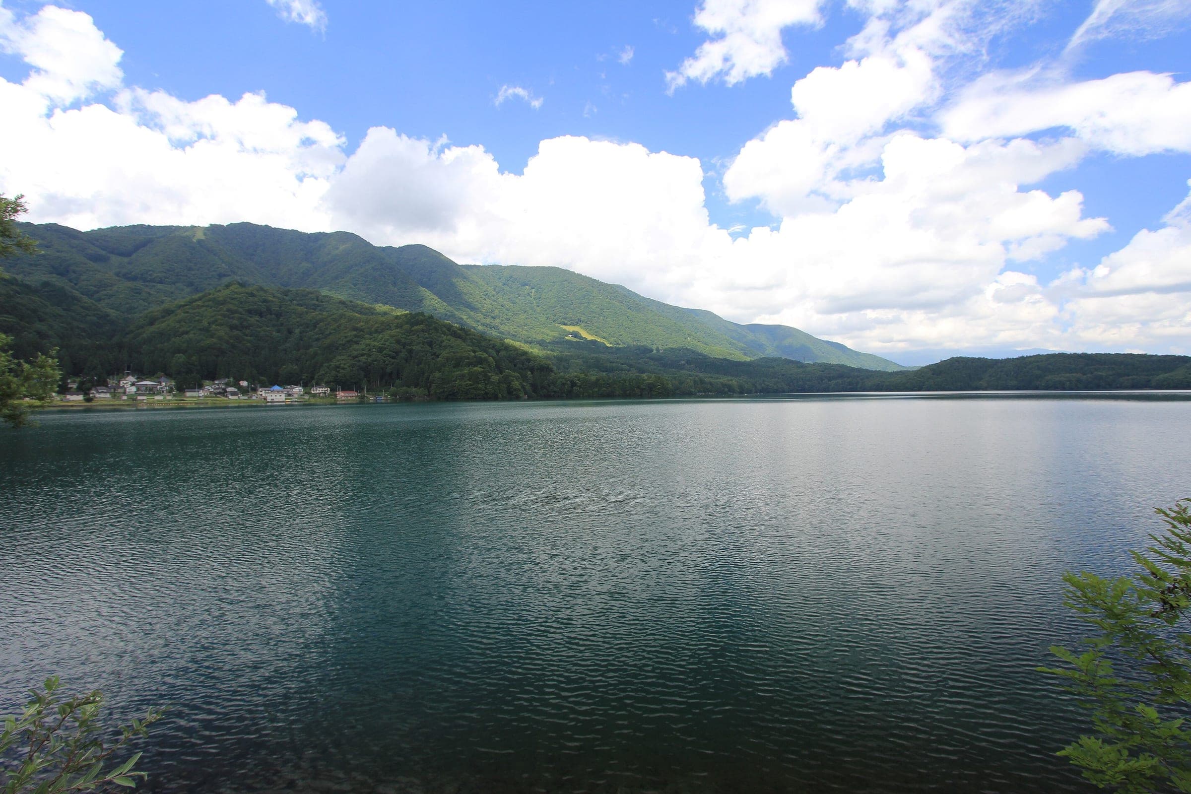 Lake Aoki lies calm under green summer mountains on the road north from Omachi toward Hakuba.