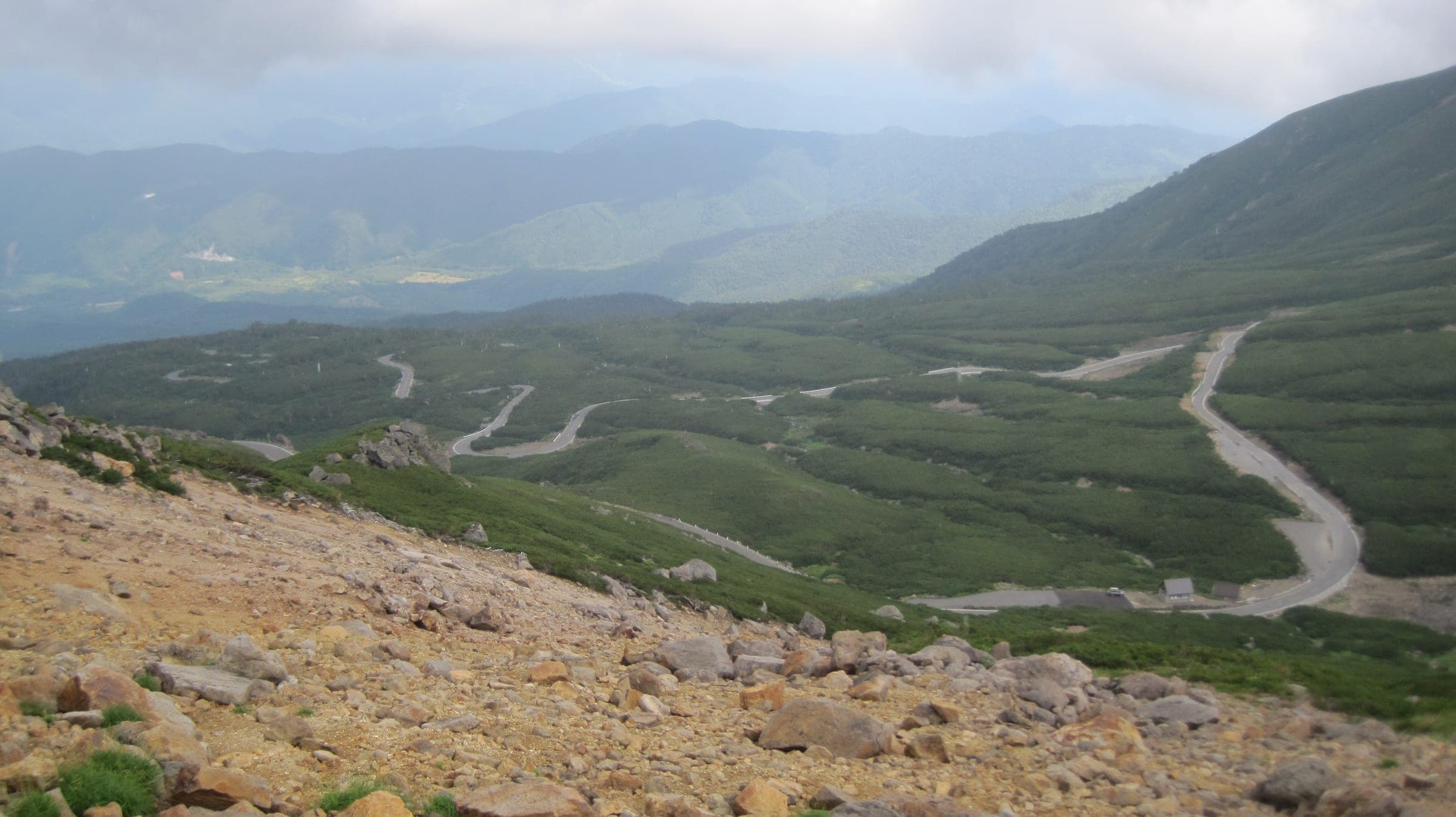 The Norikura Echo Line winds in switchbacks across the green alpine slopes below the summit ridge.