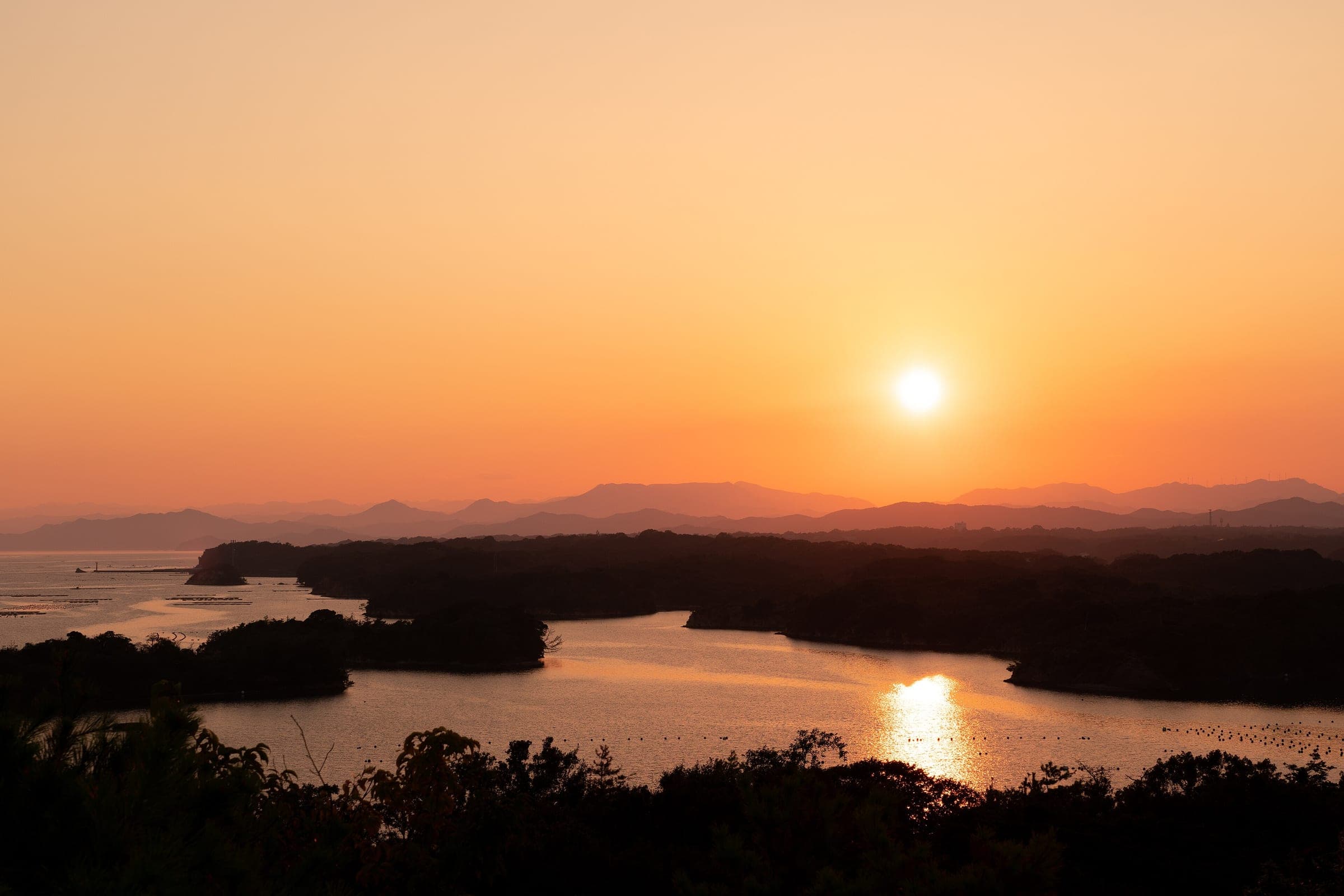 The sun drops toward the hills behind Ago Bay as the inlets catch the last light