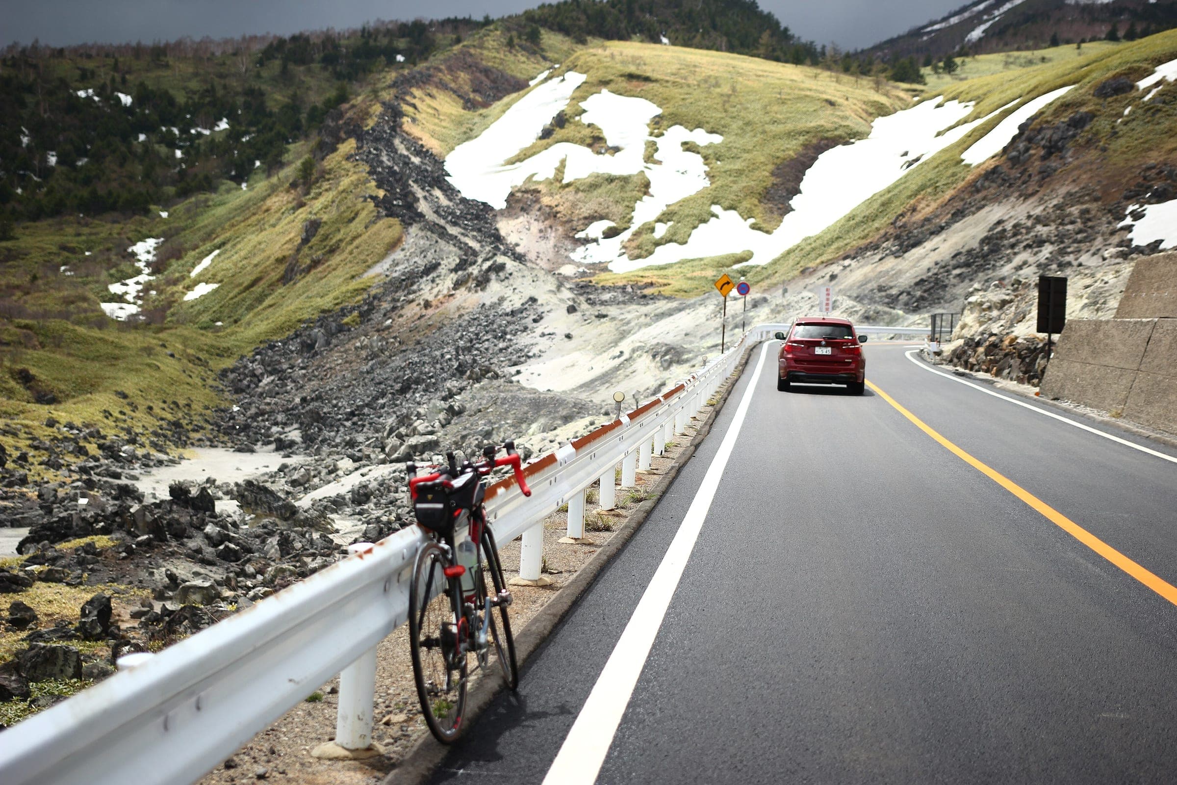 A road bike leans on the guardrail of Route 292 near Shibu Pass as late snow lingers on the slopes.