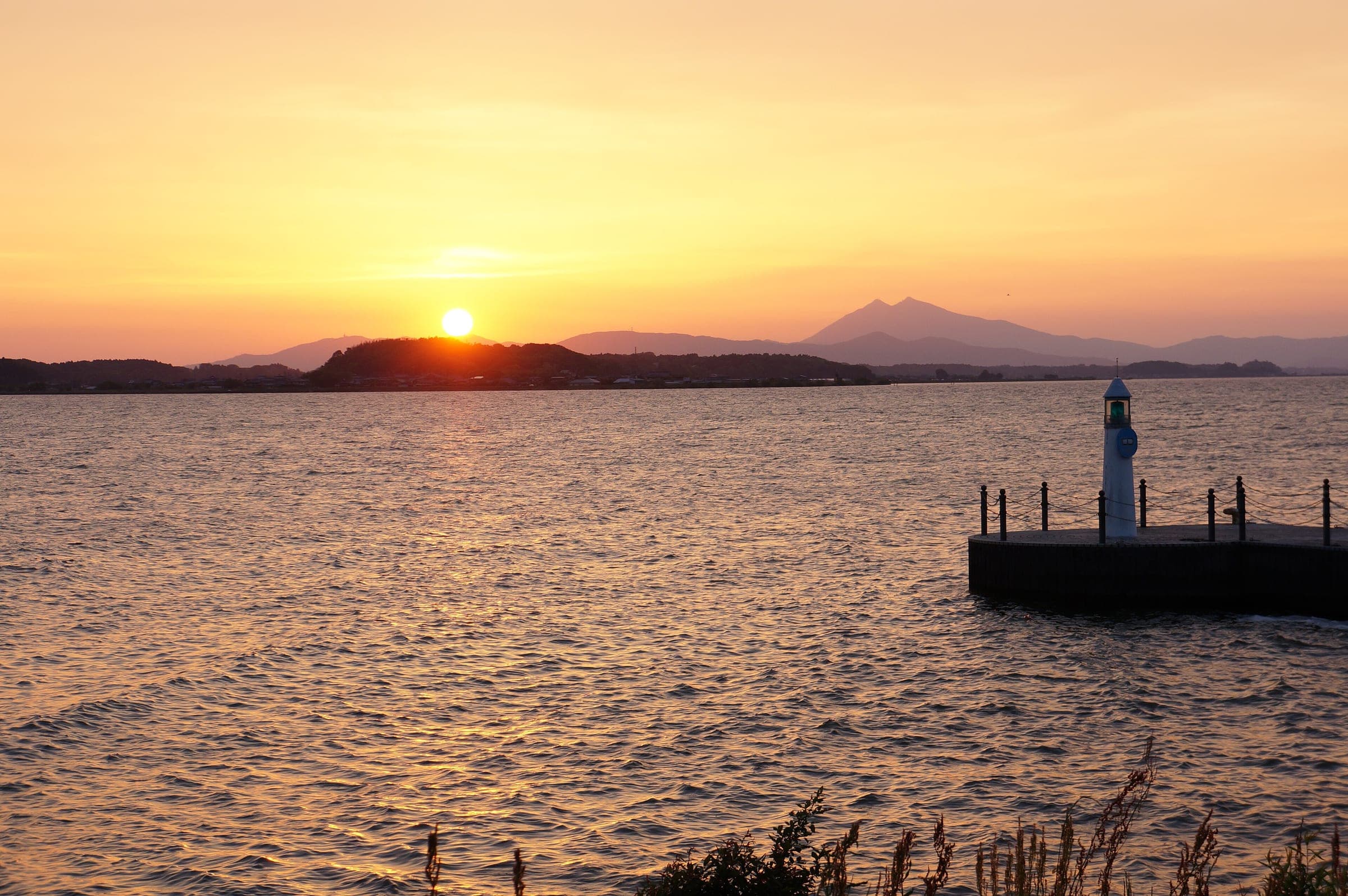 The sun sets over Lake Kasumigaura with the twin peaks of Mt. Tsukuba on the far shore.