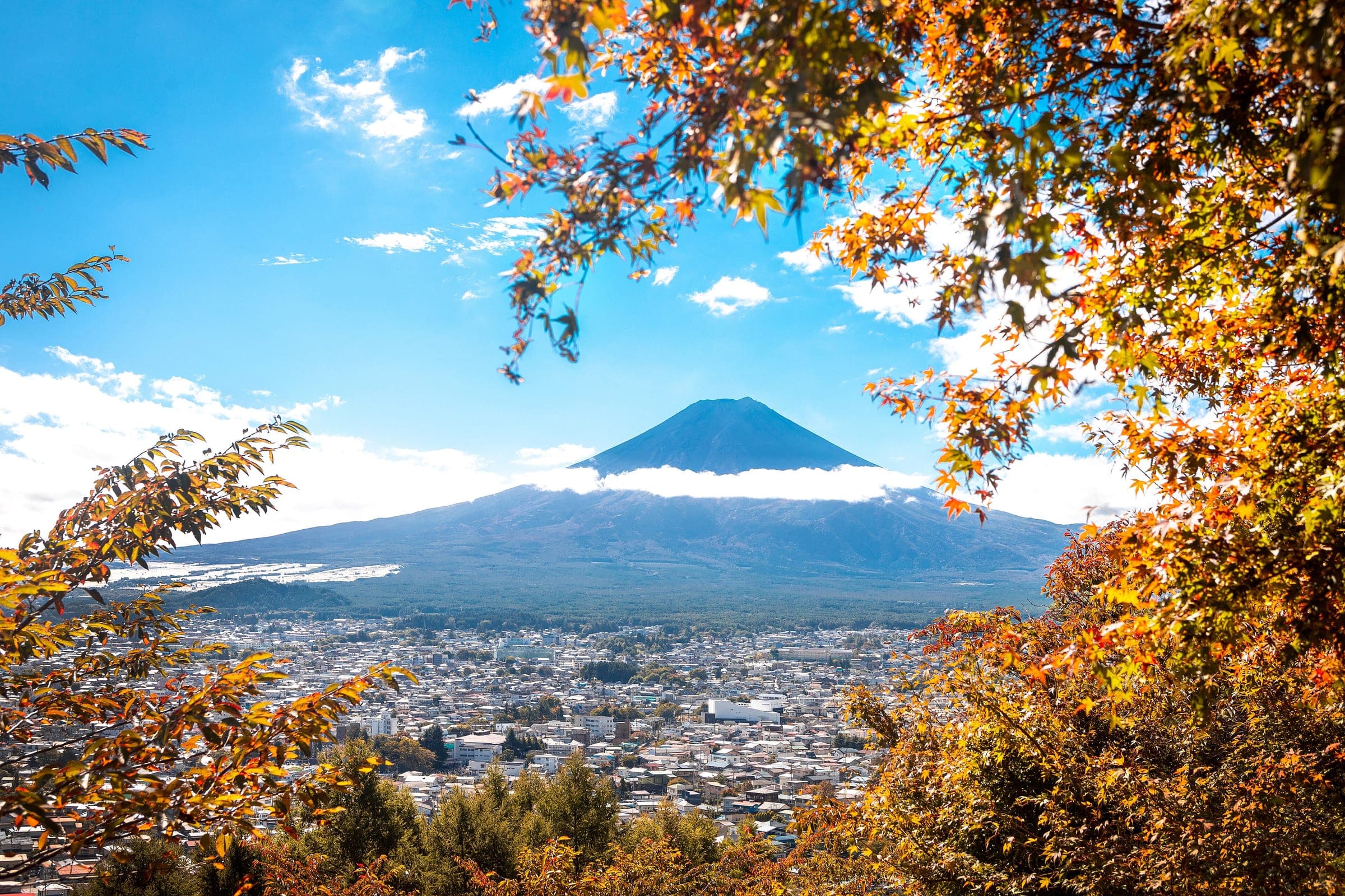 Autumn leaves frame Mt. Fuji and the rooftops of Fujiyoshida from the slopes of Arakurayama Sengen Park.
