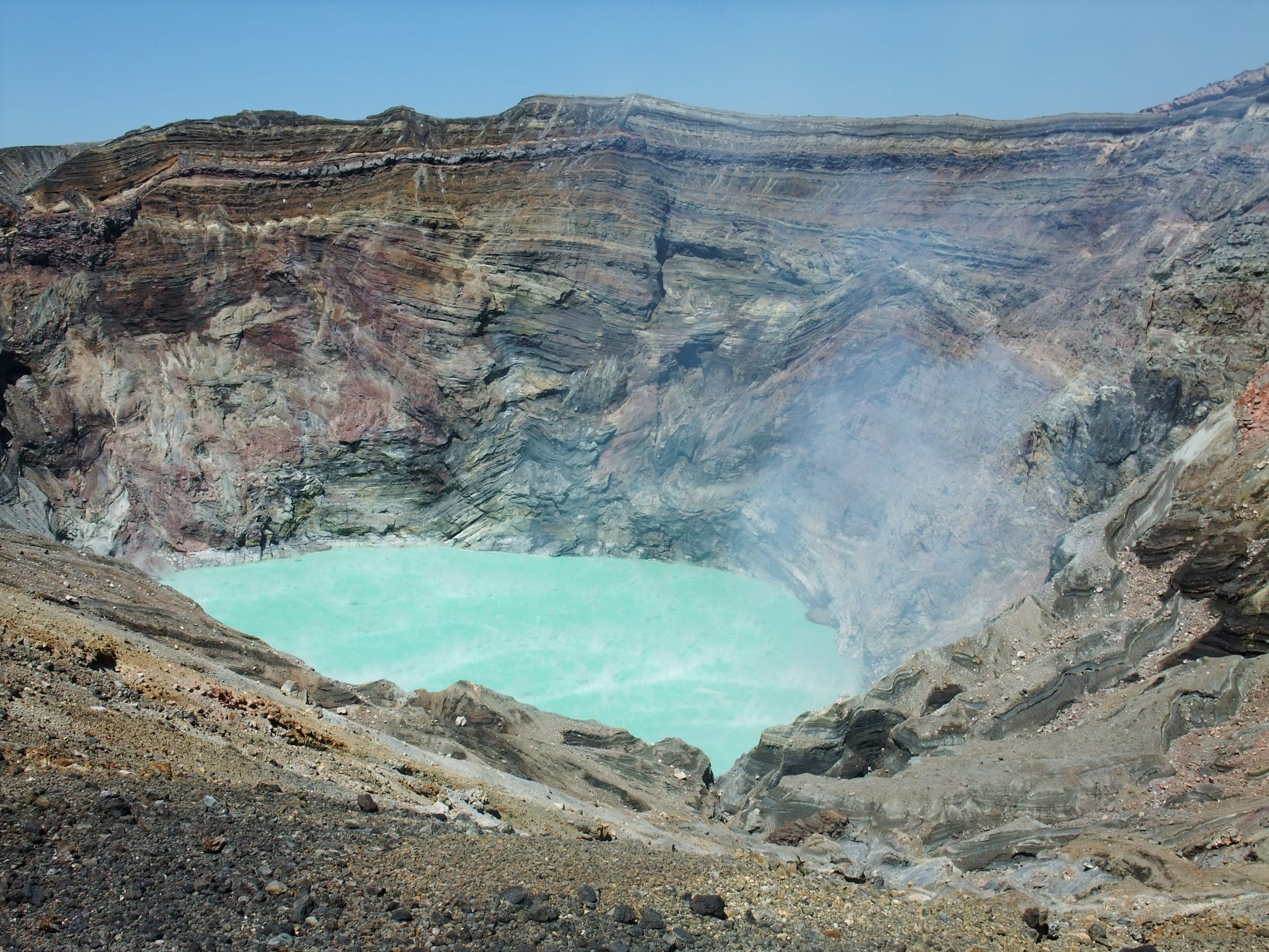 A turquoise acid lake steams at the bottom of the layered walls of Aso's Nakadake crater.