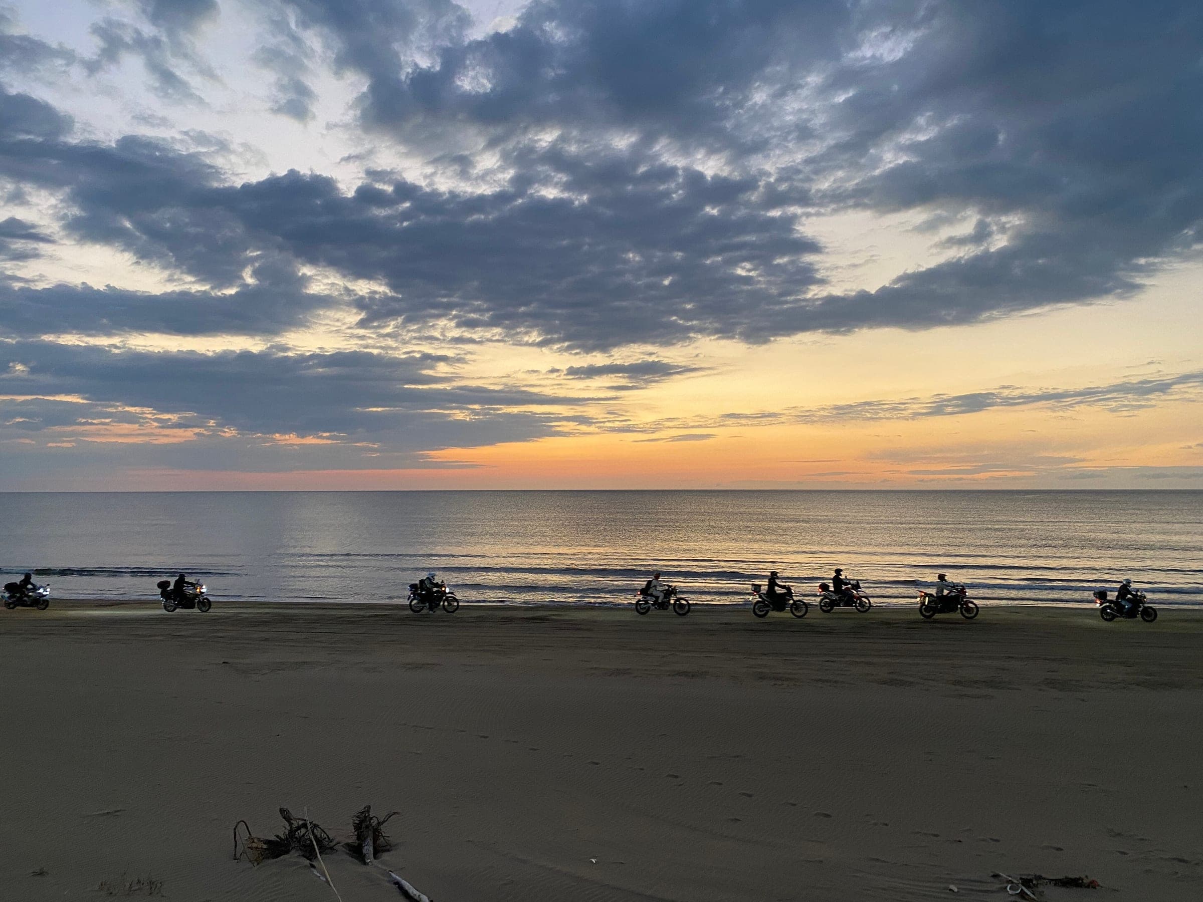 Motorcyclists ride along the sand of the Chirihama Nagisa Driveway as the sun sets over the Sea of Japan