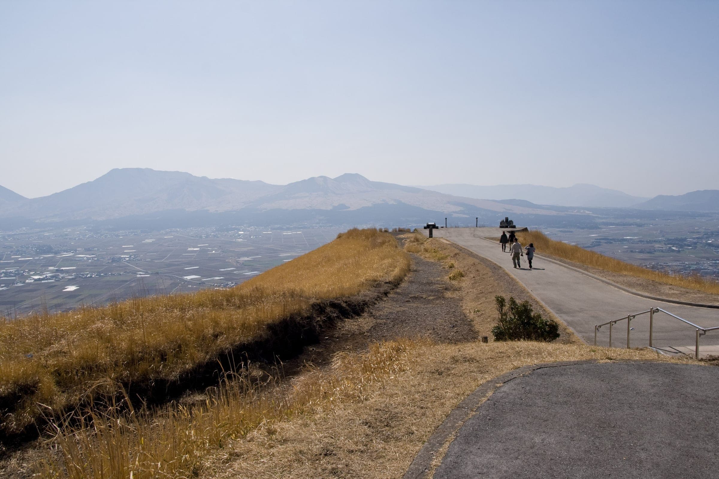 Walkers follow the paved path along the Daikanbo ridge above the Aso caldera in late winter.
