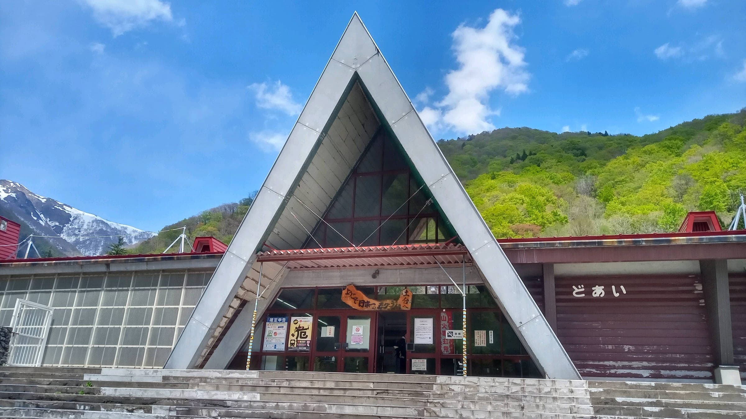 Doai Station's A-frame building stands below green slopes and a snowy ridge in May