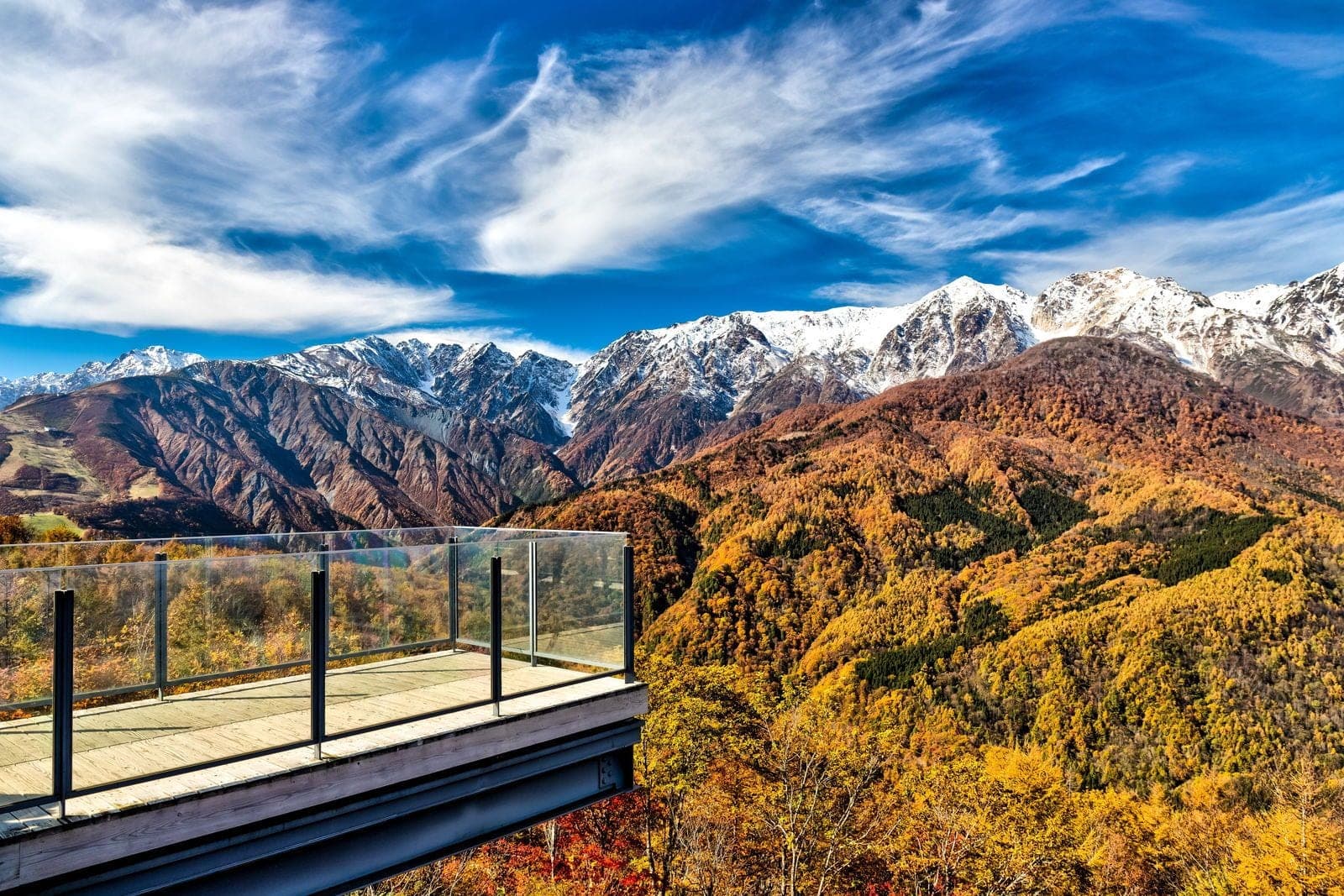 A glass-railed viewing deck on Hakuba Iwatake juts out toward the white Northern Alps in late October.