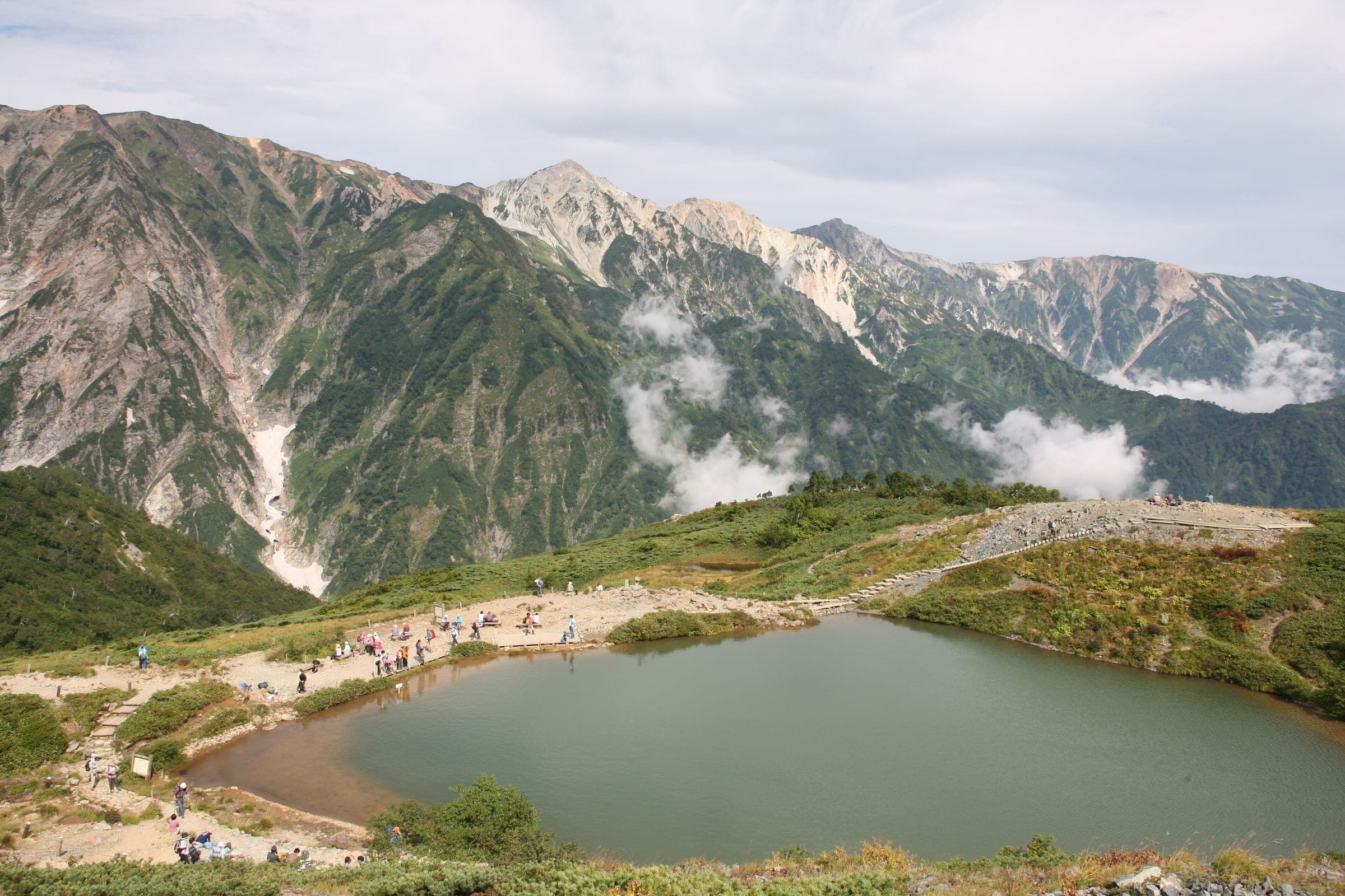 Walkers circle Happo-ike Pond on the Happo-one ridge below the Hakuba Sanzan peaks in summer.