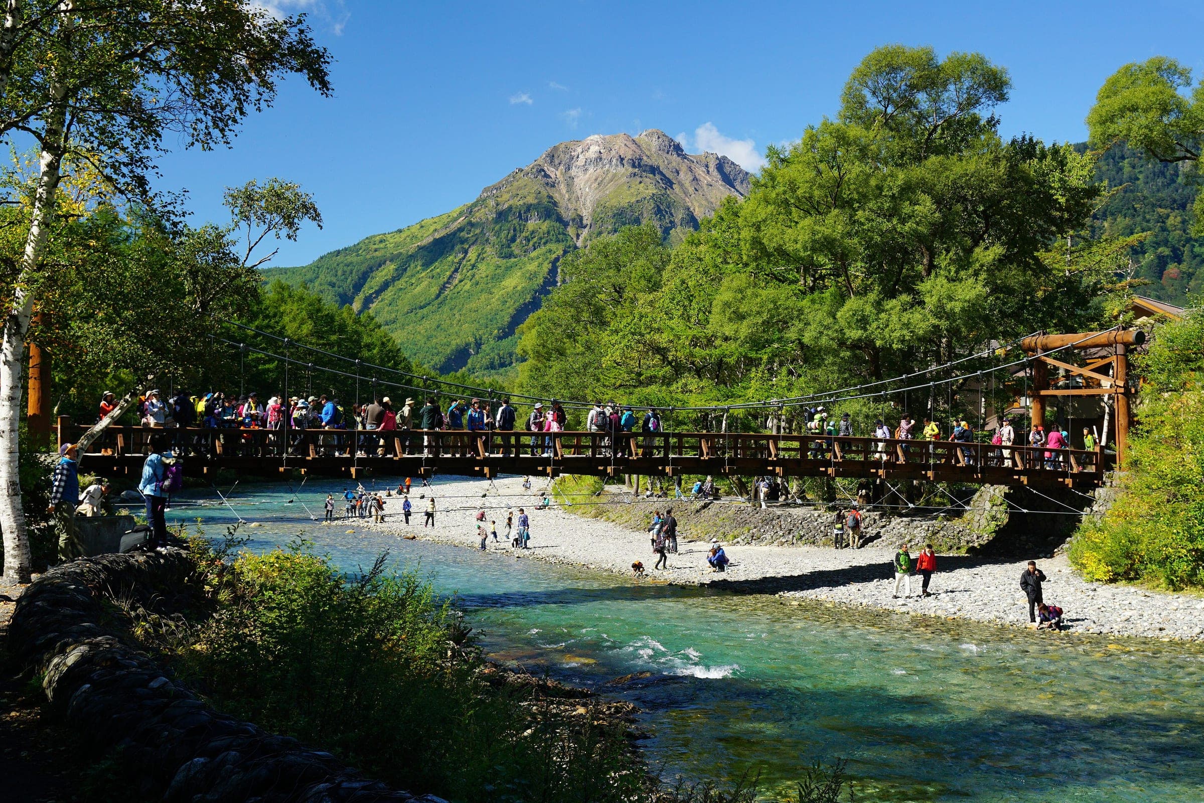 Walkers cross the Kappa-bashi suspension bridge over the Azusa River at Kamikochi under Mount Yake.