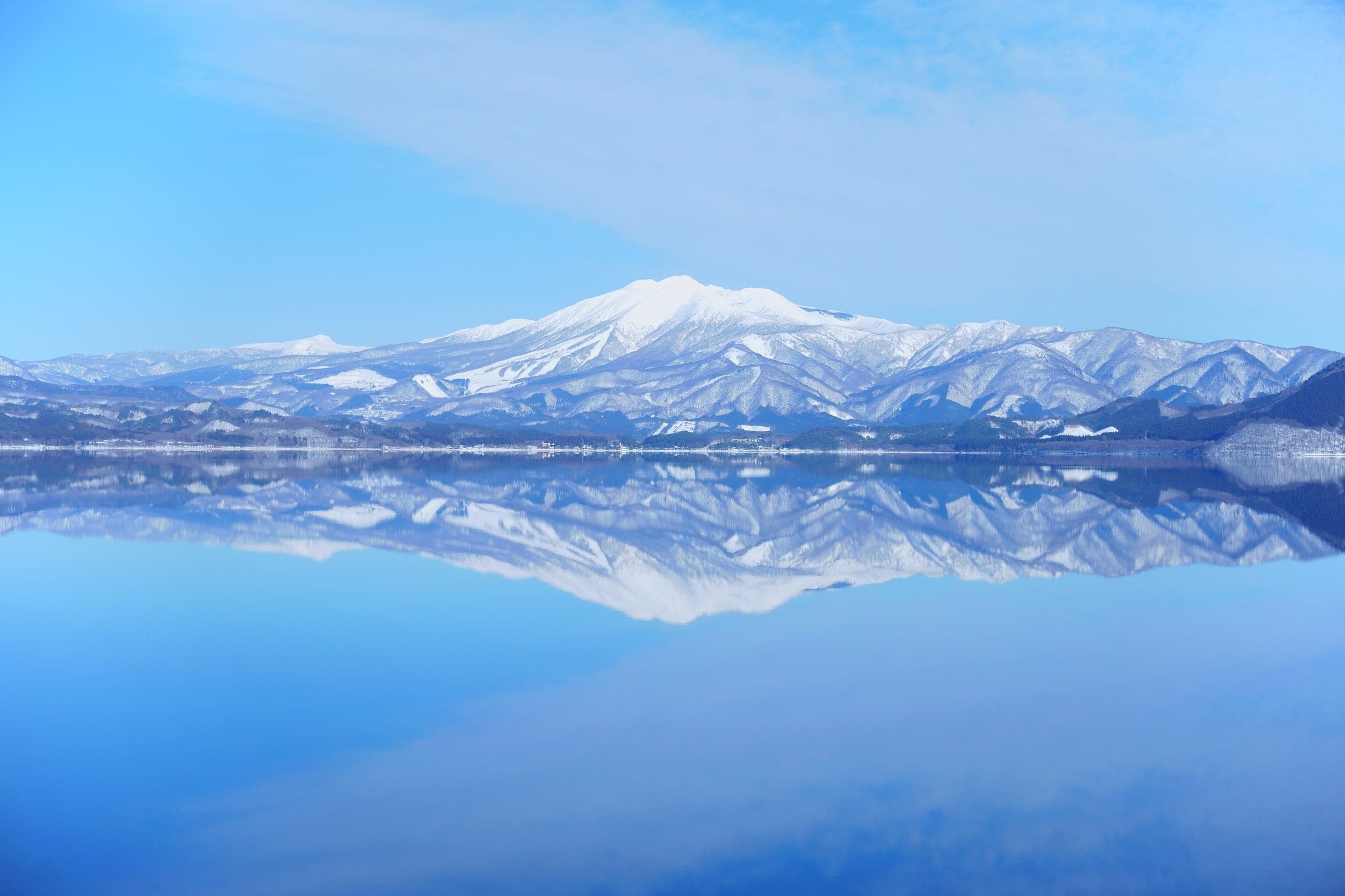 Mount Akita-Komagatake reflects in the calm surface of Lake Tazawa on a clear February day.