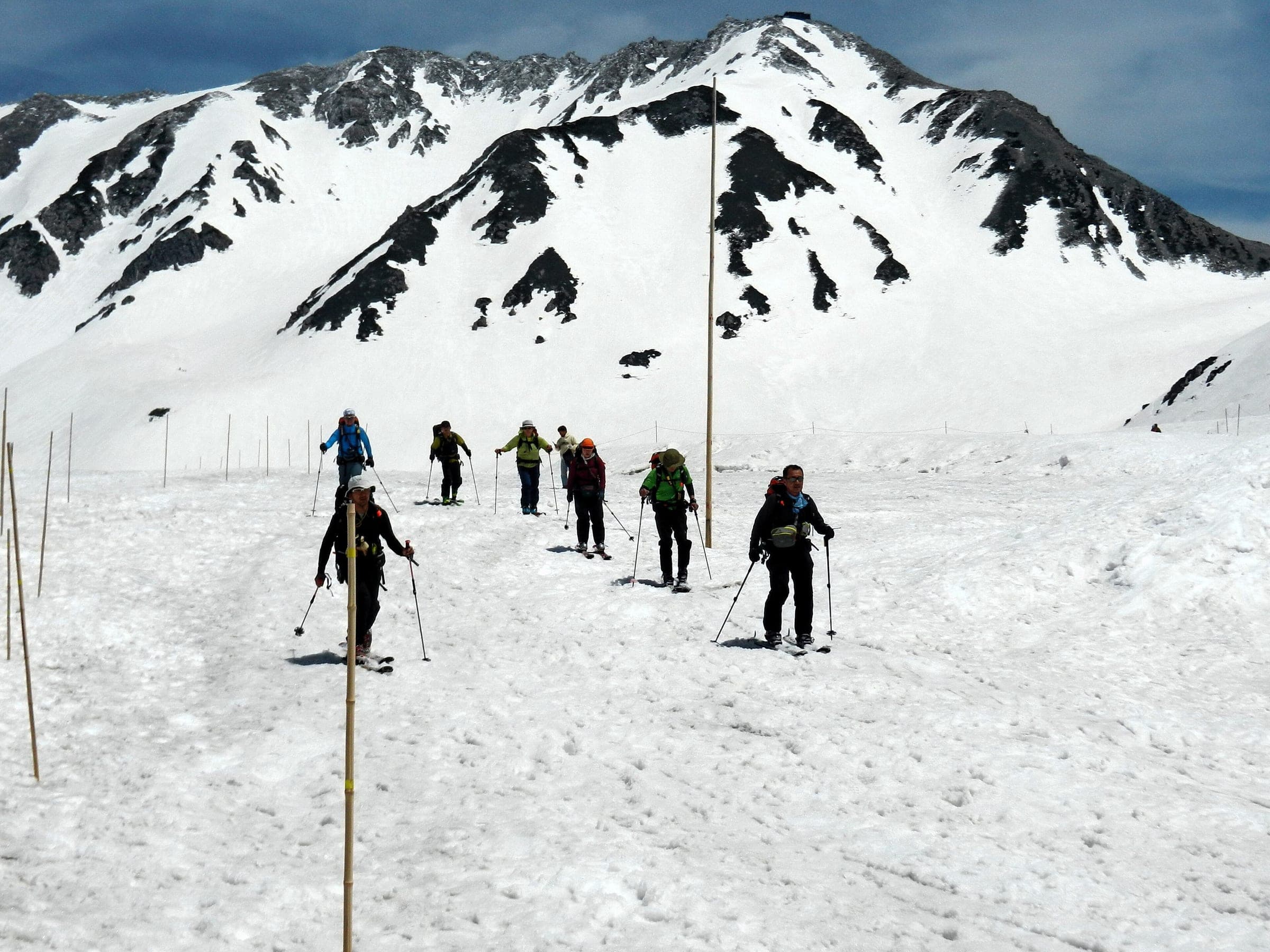 Ski tourers follow a line of marker poles across the spring snow at Murodo under the Tateyama peaks