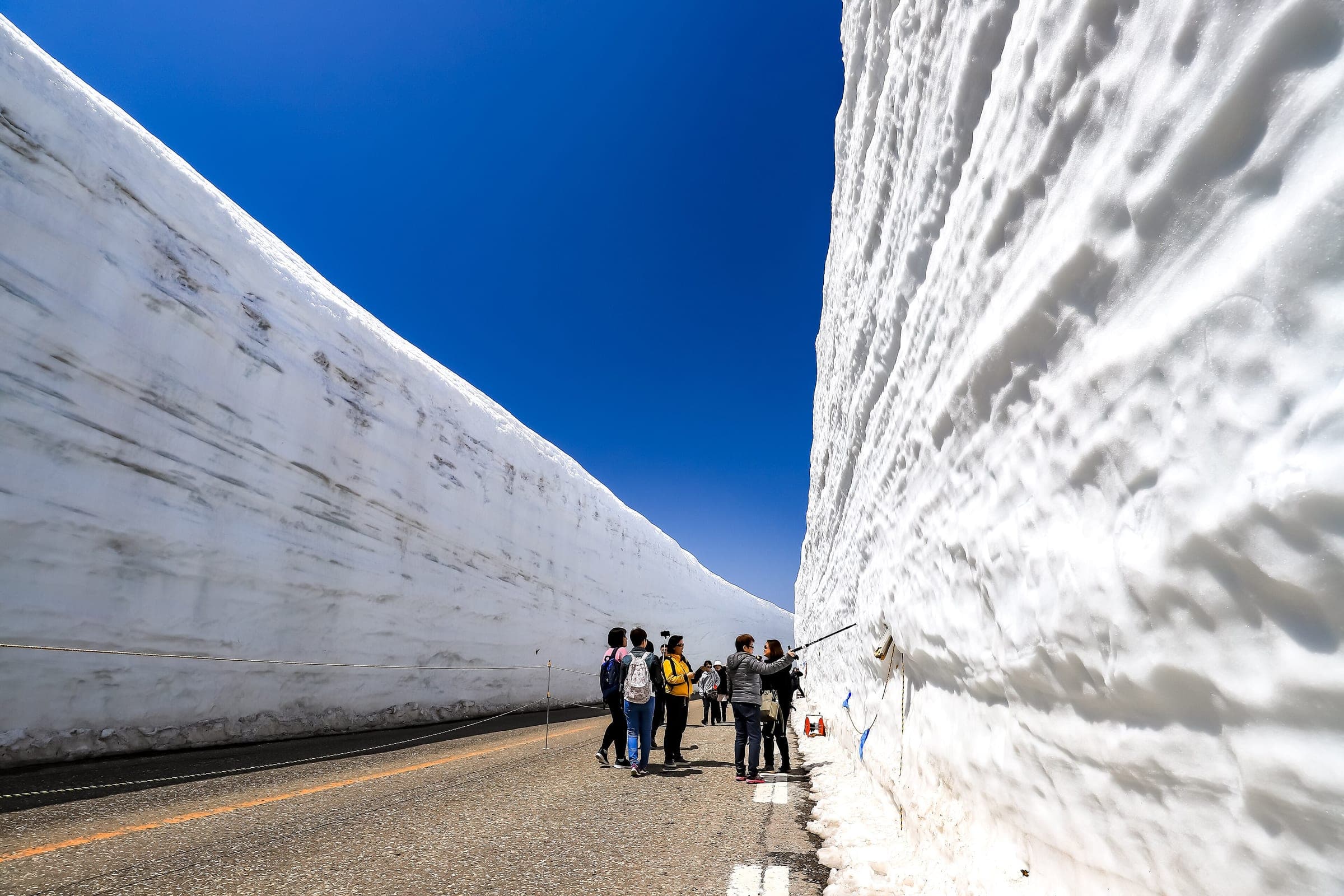 Visitors walk between the towering snow walls of Yuki-no-Otani on the road at Murodo in April
