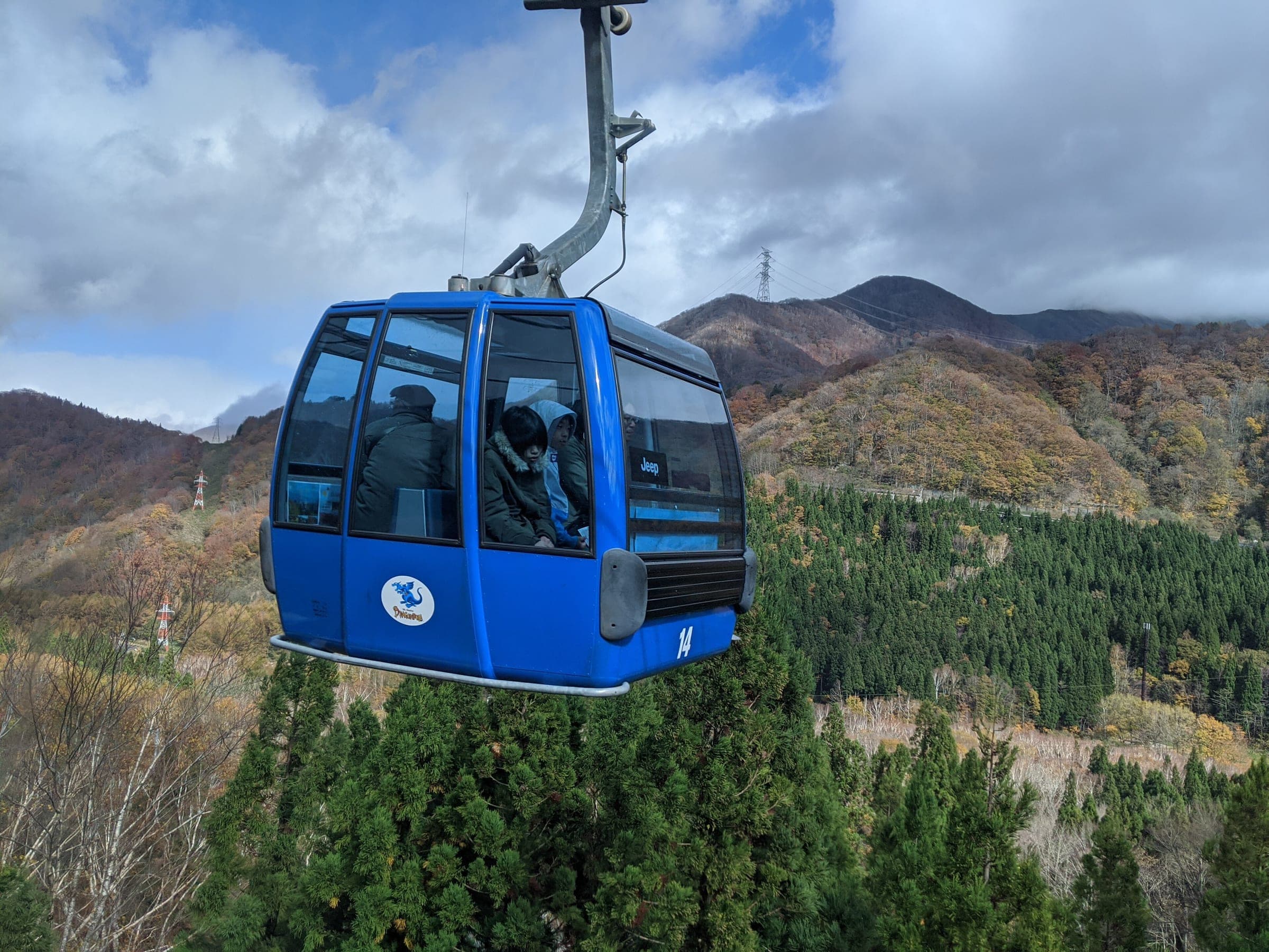 A blue Dragondola cabin glides over autumn forest above Naeba in early November